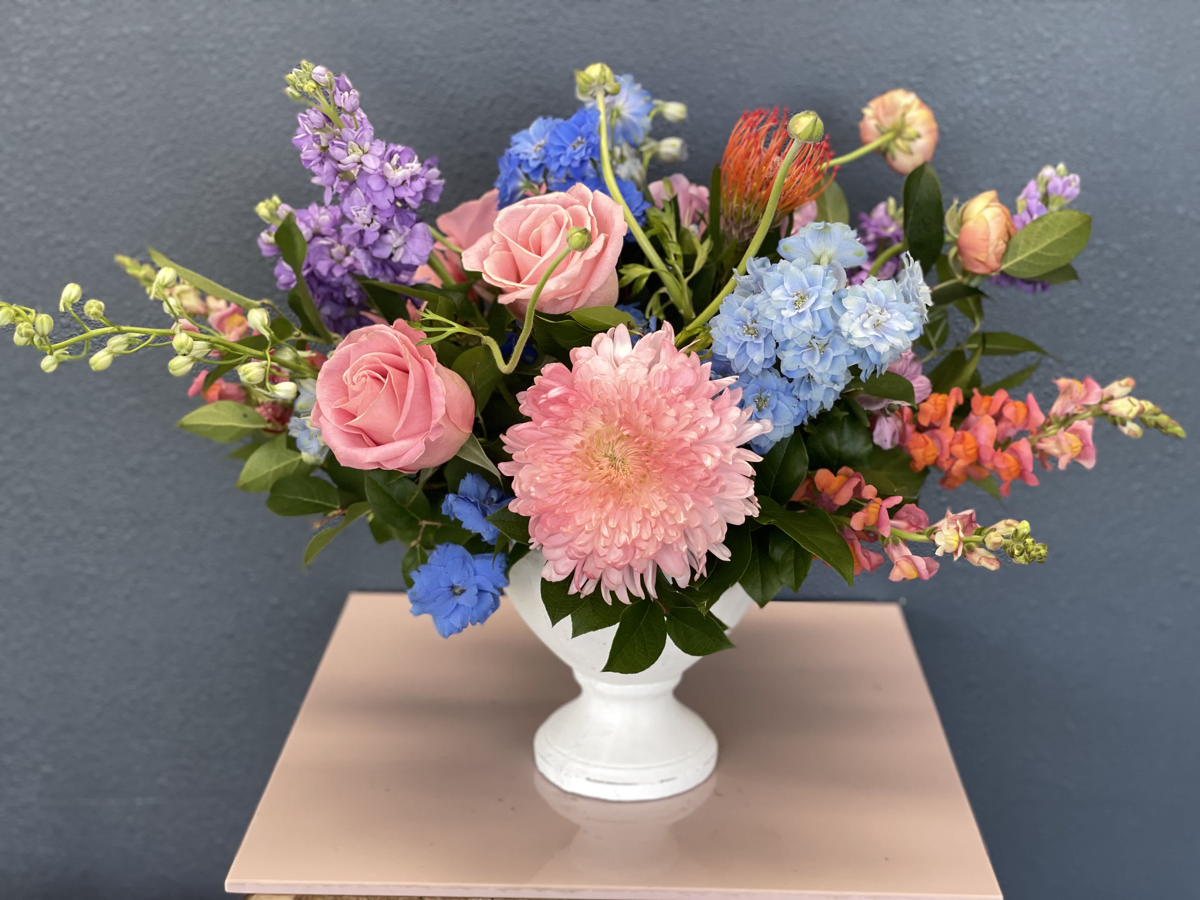 Mixed bouquet of pink roses, blue hydrangeas, and purple blooms in a white vase