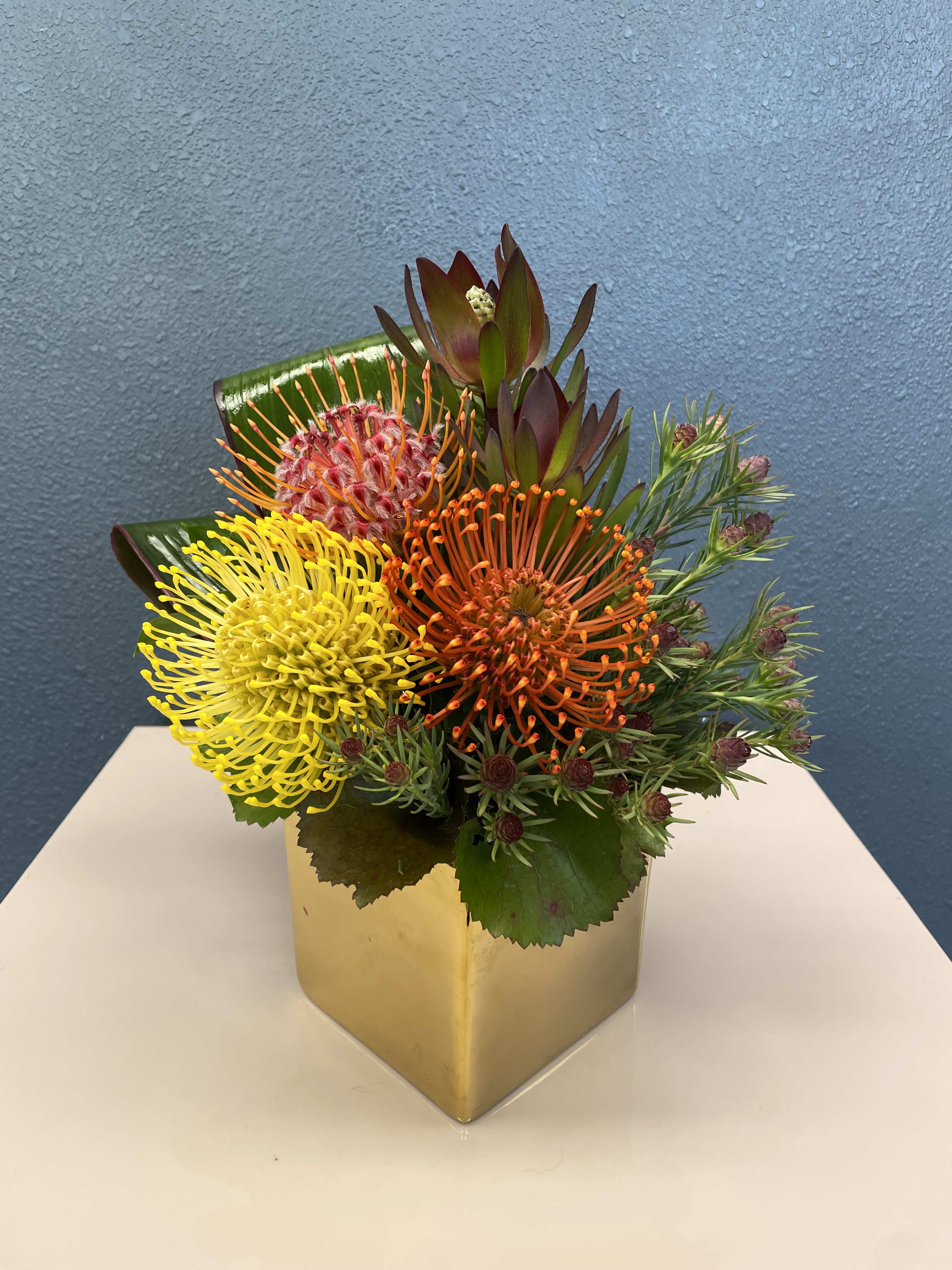Bright mixed bouquet in a gold square vase with yellow and orange blooms