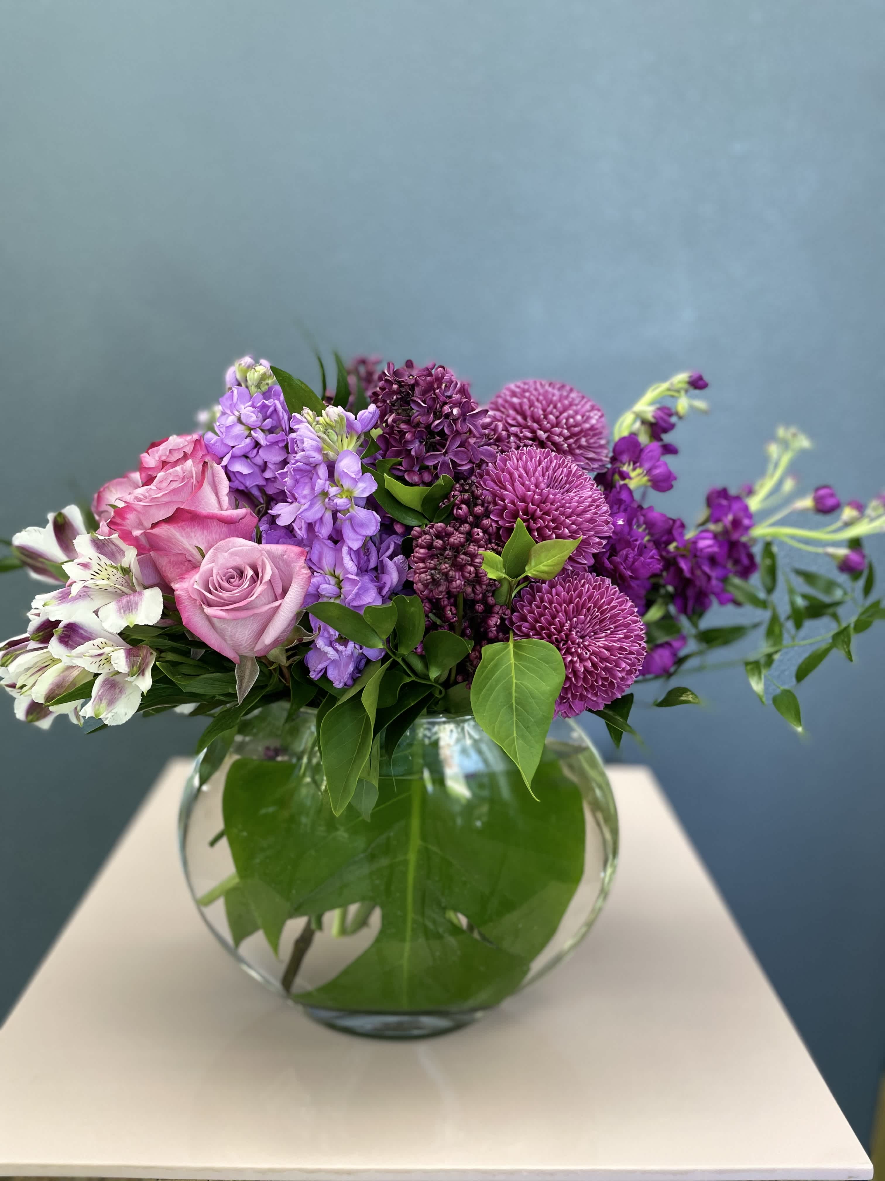 Pink and purple flowers arranged in a round glass vase