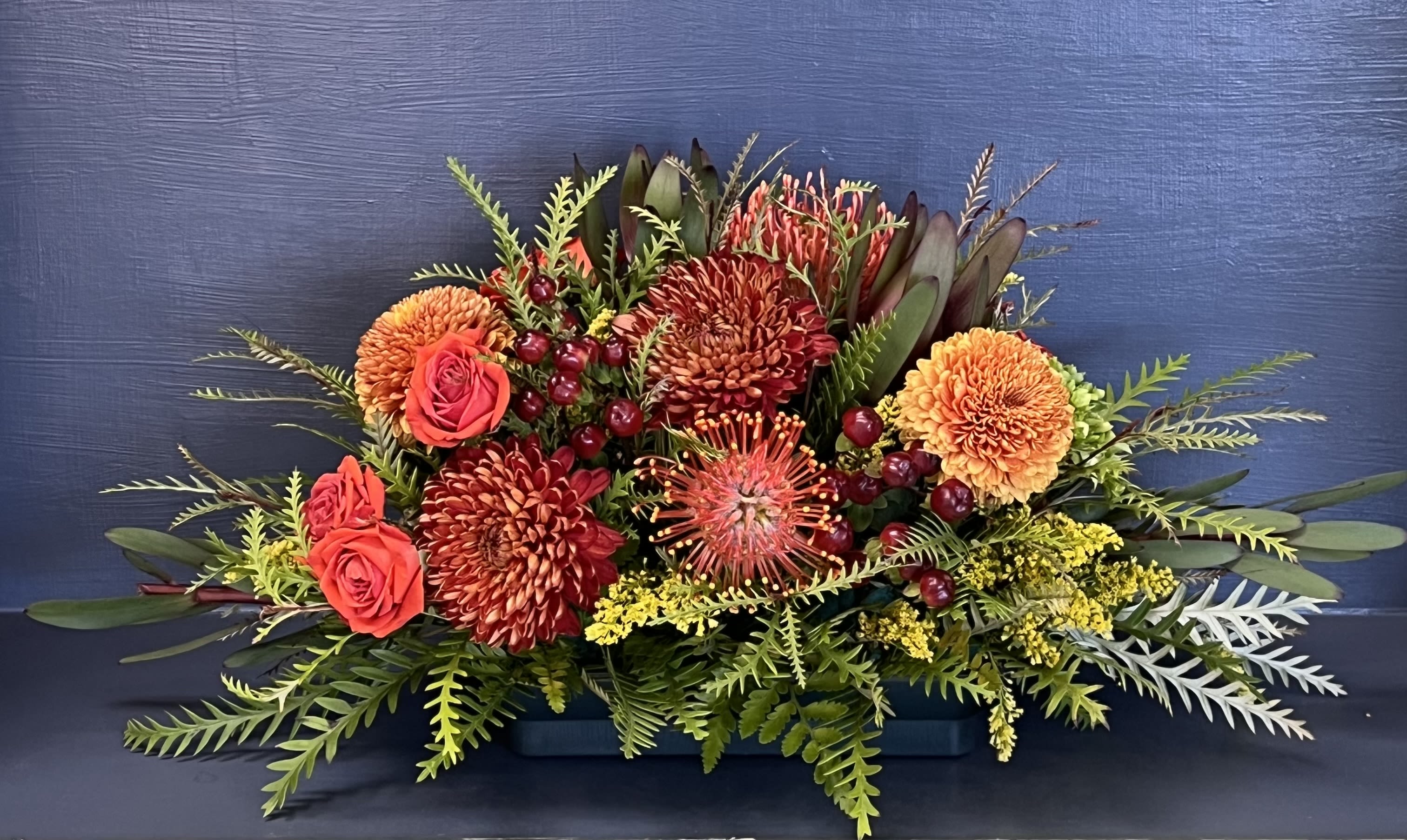 Low floral arrangement with orange and red blooms in a rectangular container