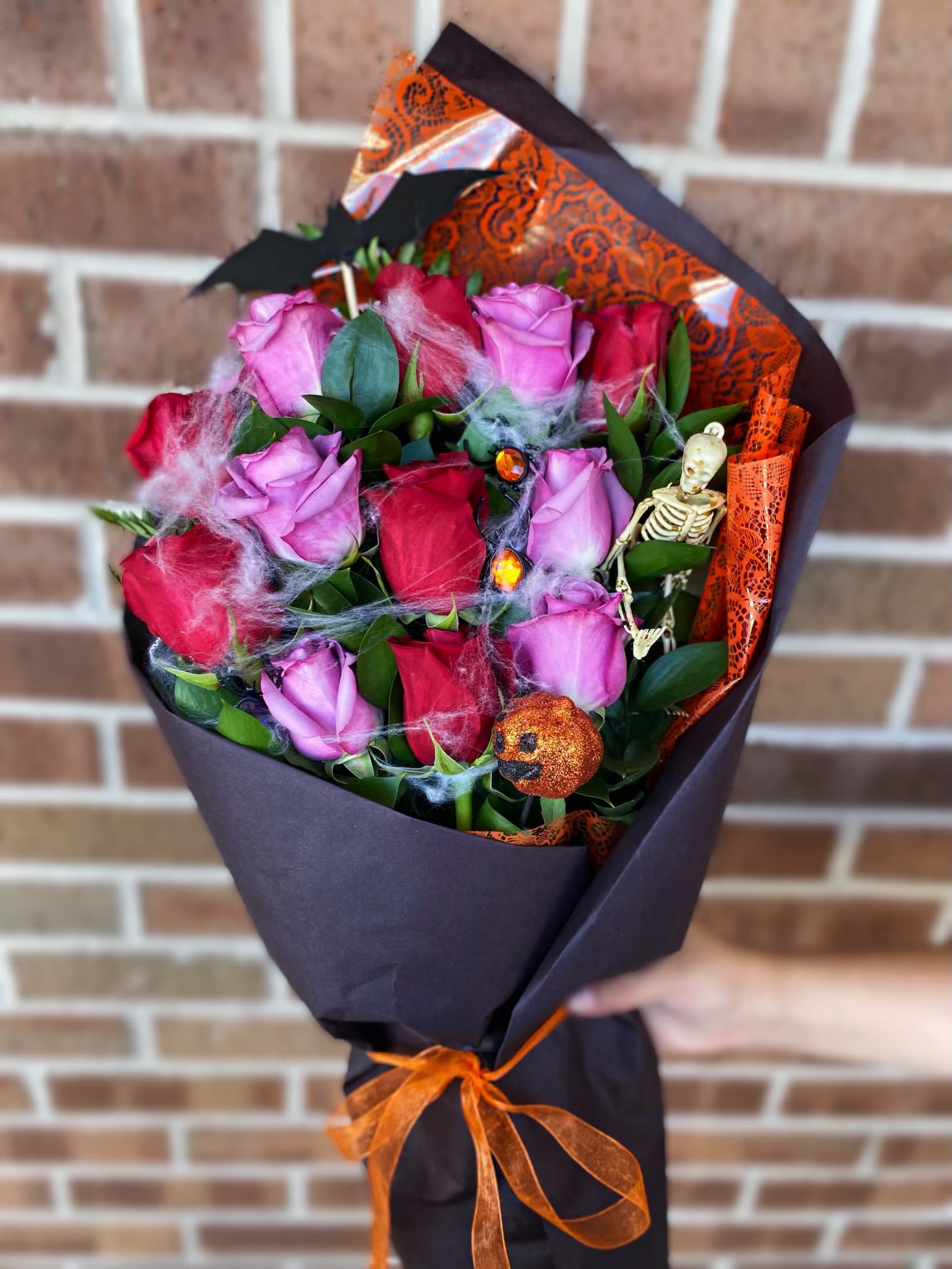 Bouquet of pink and red roses wrapped in black paper with orange ribbon