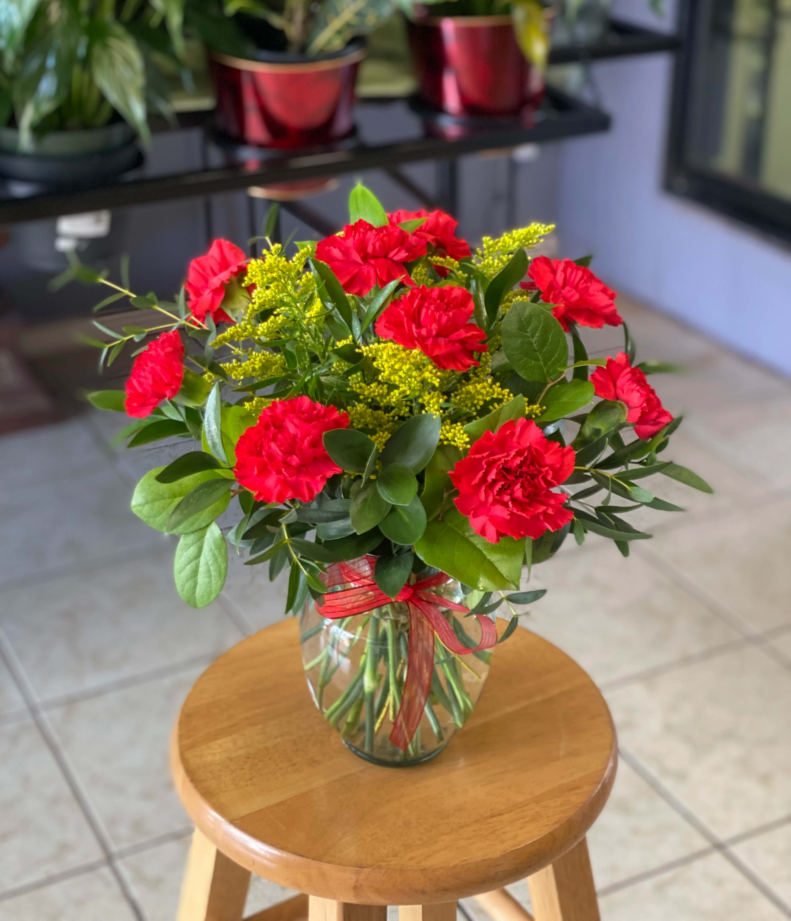 Red carnations in a glass vase with yellow filler flowers