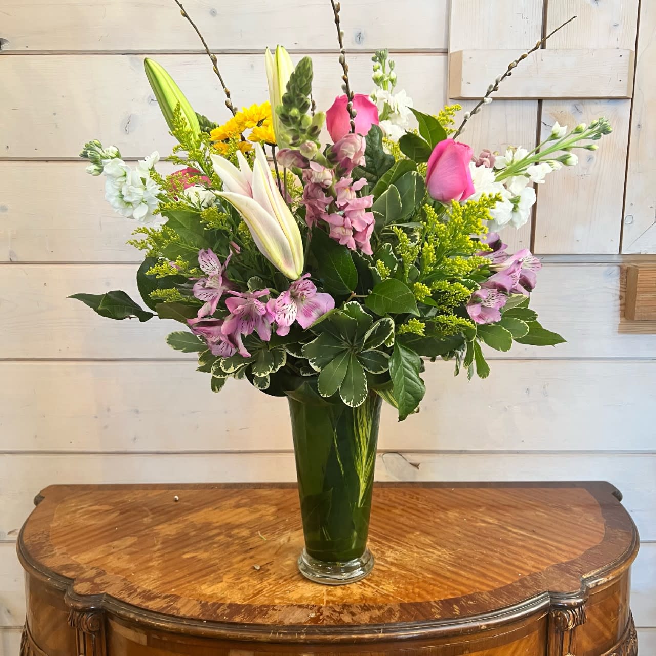 Mixed bouquet of lilies, roses, and alstroemeria in a green glass vase
