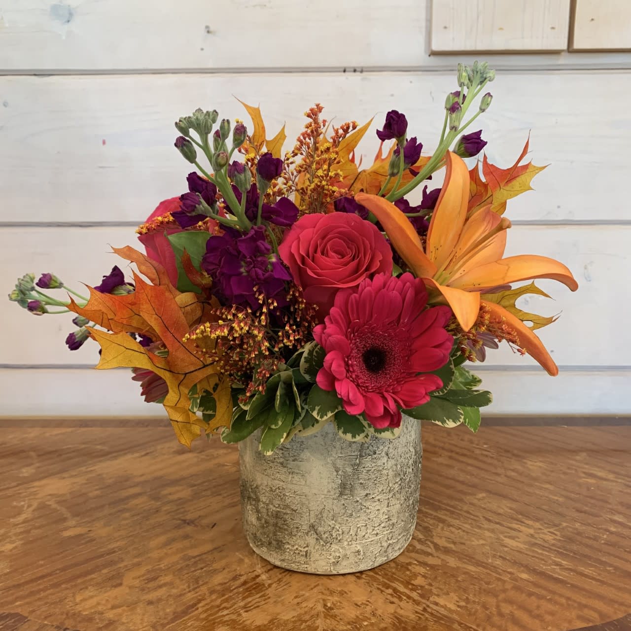 Bright mixed flower arrangement in a textured gray vase with orange leaves