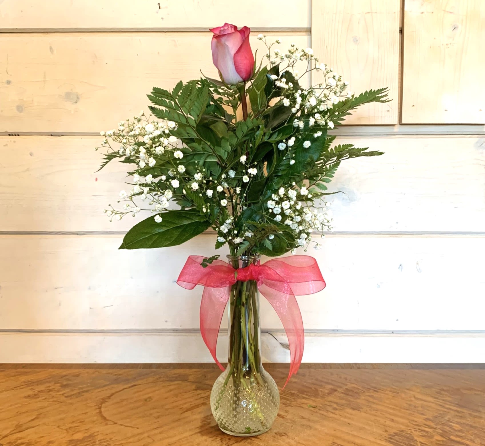 Single pink rose in a glass vase with baby's breath and a pink ribbon