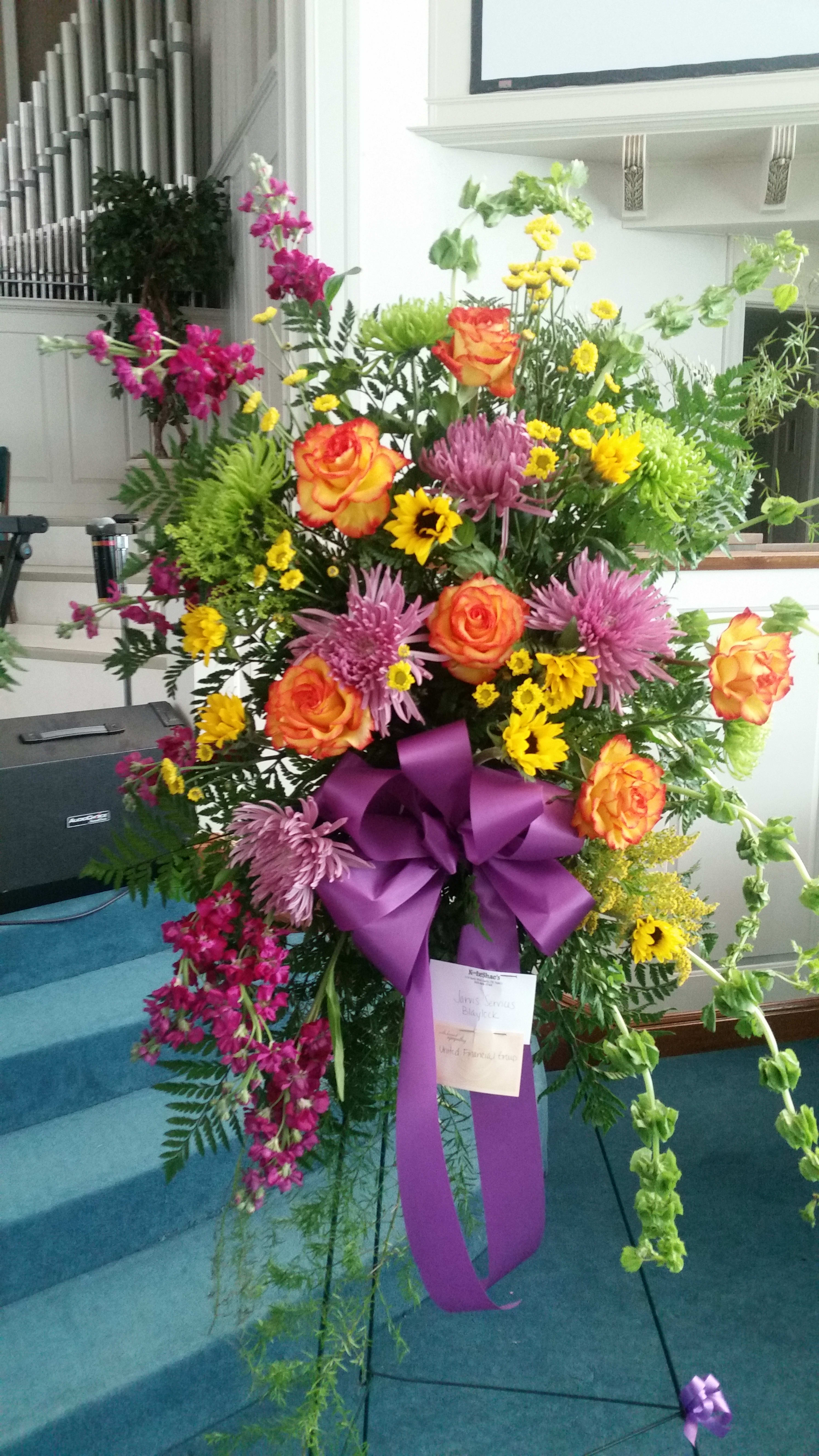 Tall floral standing spray with orange roses, purple mums, and yellow daisies