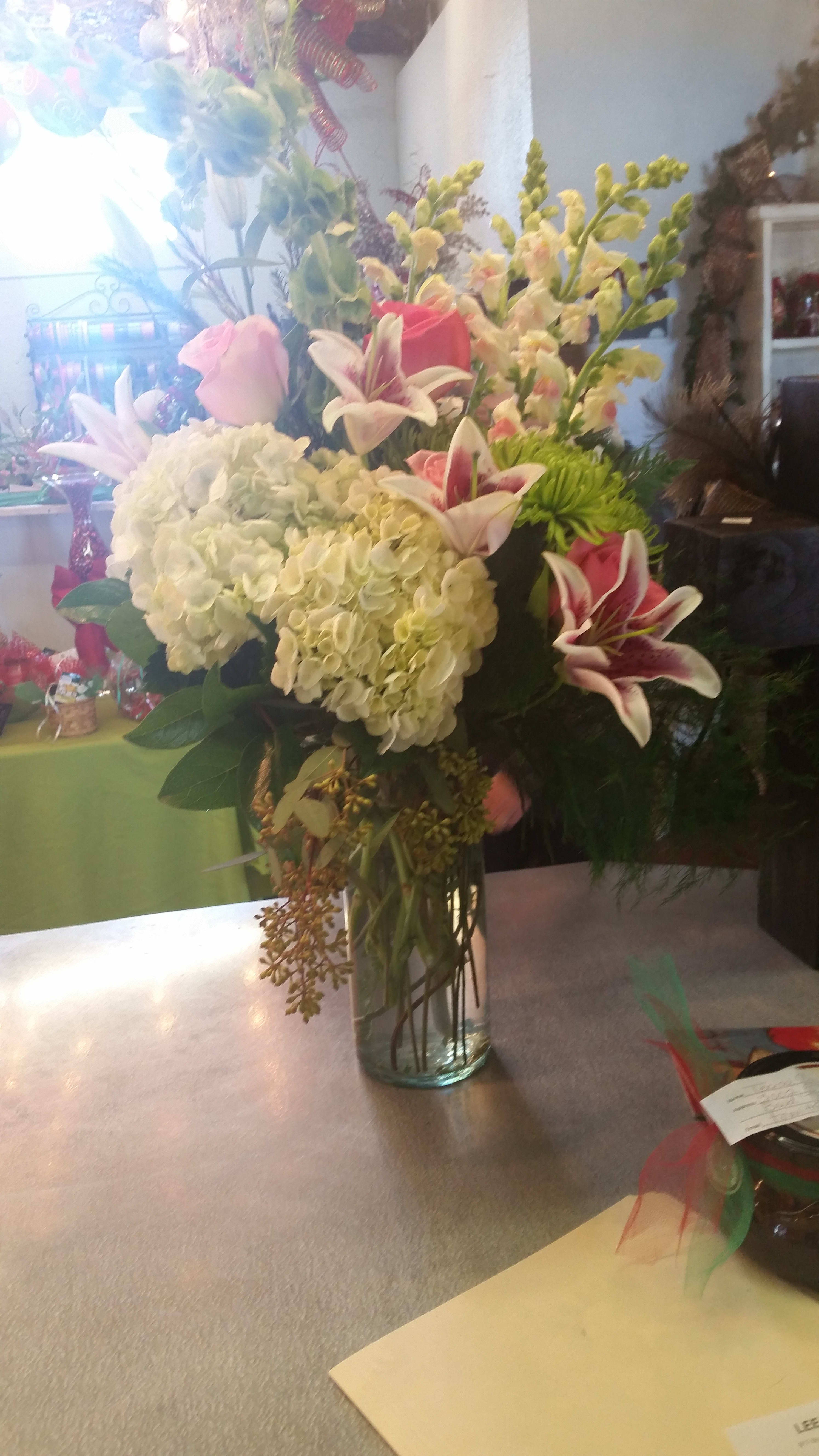 Tall bouquet of white hydrangeas, pink roses, and lilies in a glass vase
