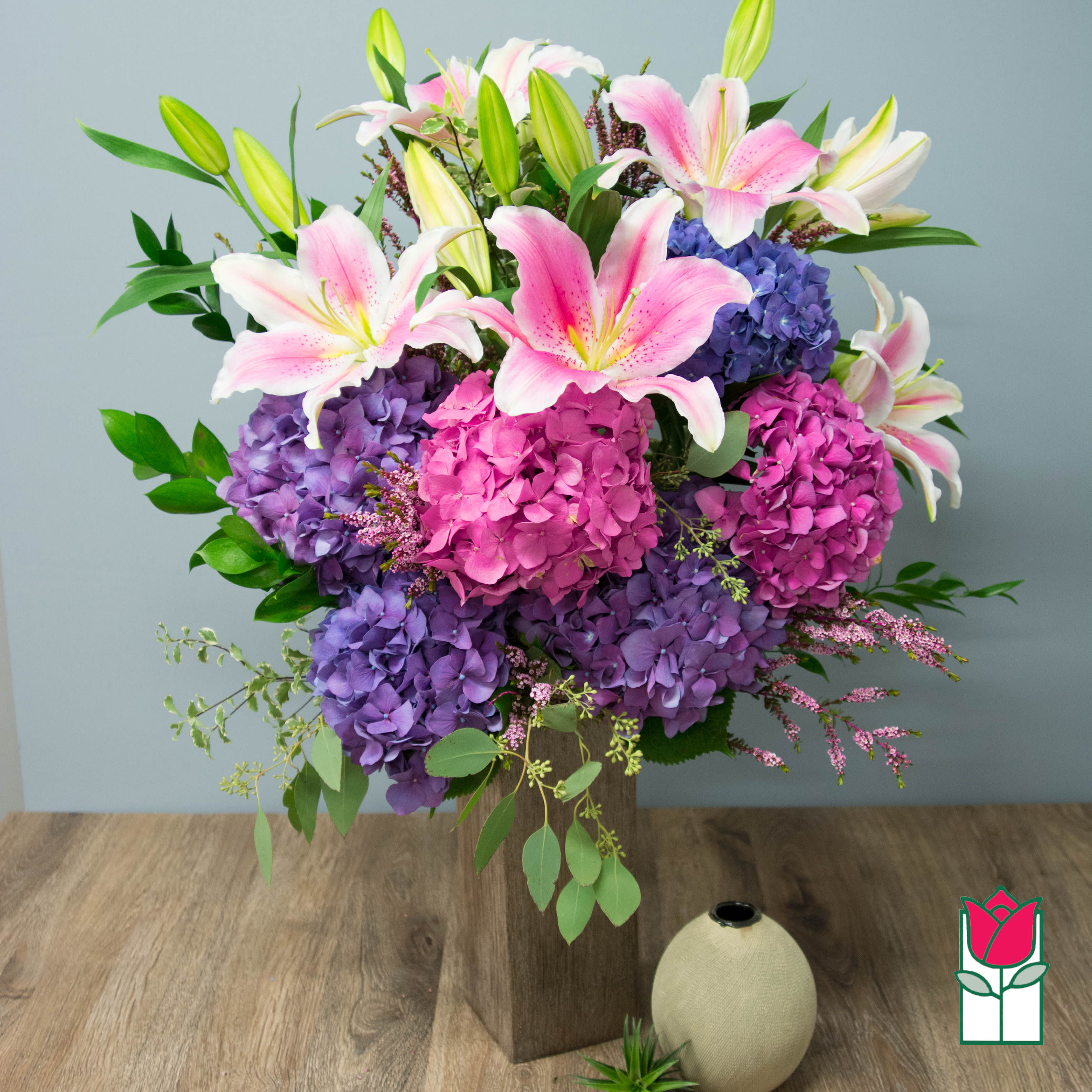 Pink lilies and purple hydrangeas arranged in a wooden vase
