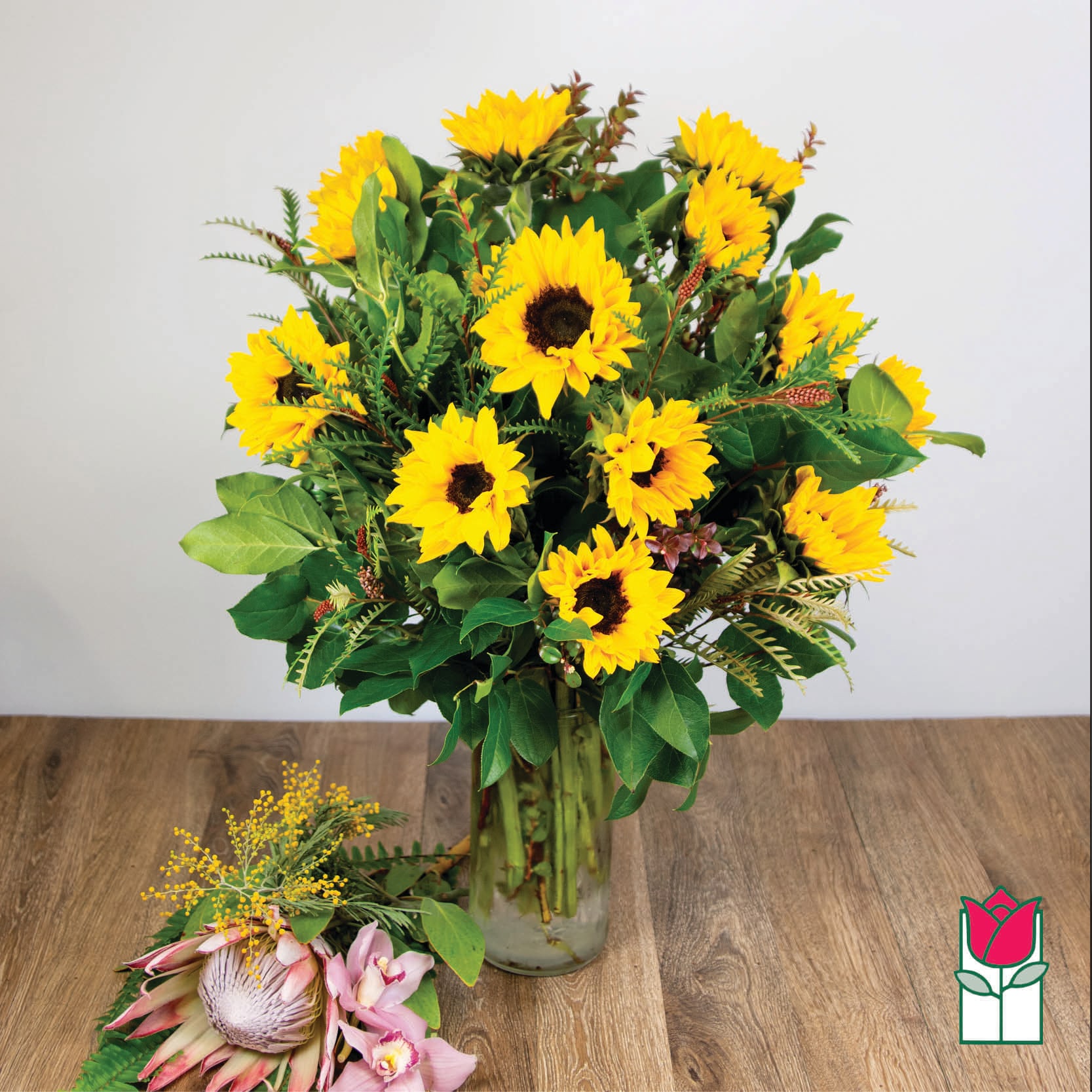 Sunflower bouquet in a clear glass vase with a small pink tropical flower cluster beside it