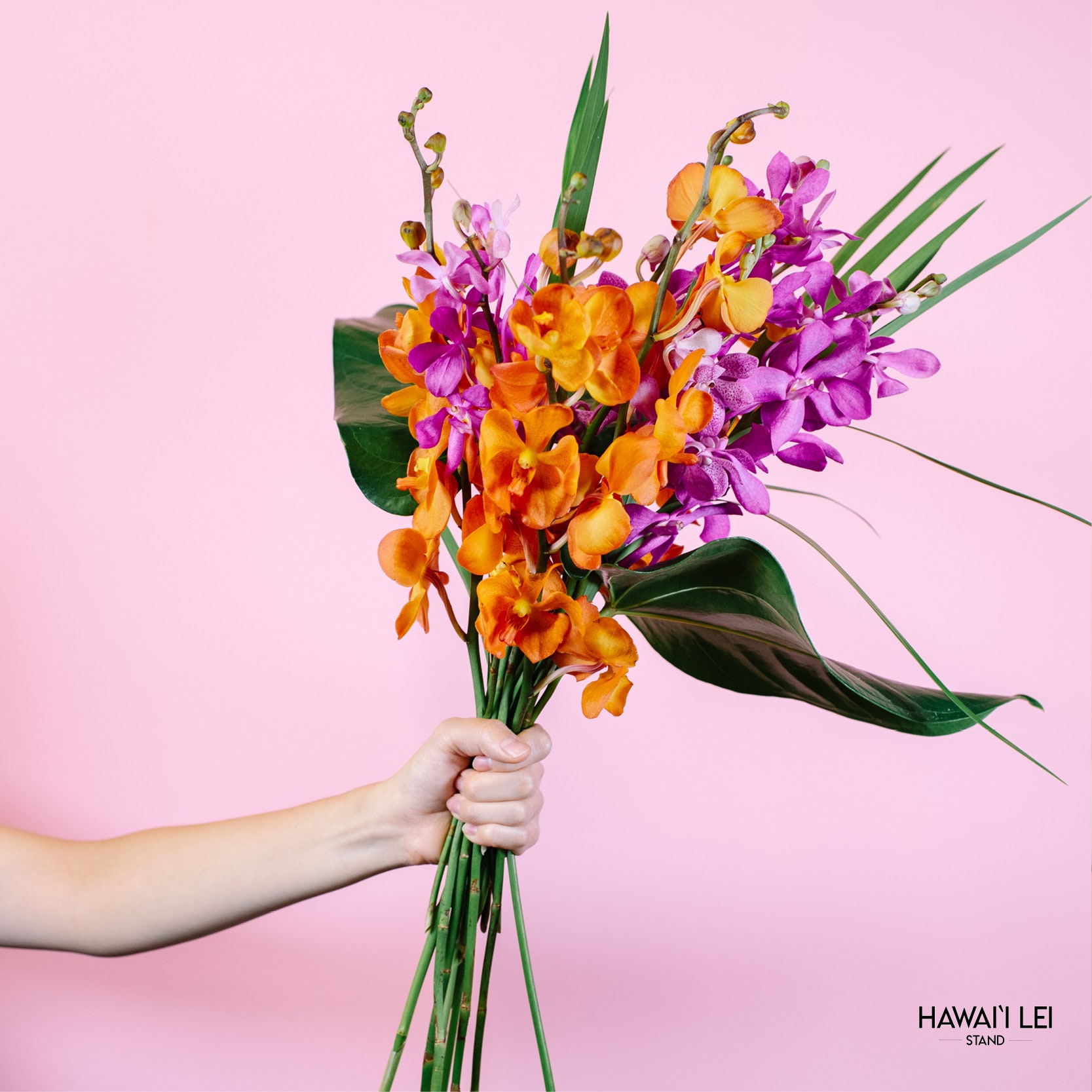 Handheld bouquet of orange and purple orchids with tropical leaves