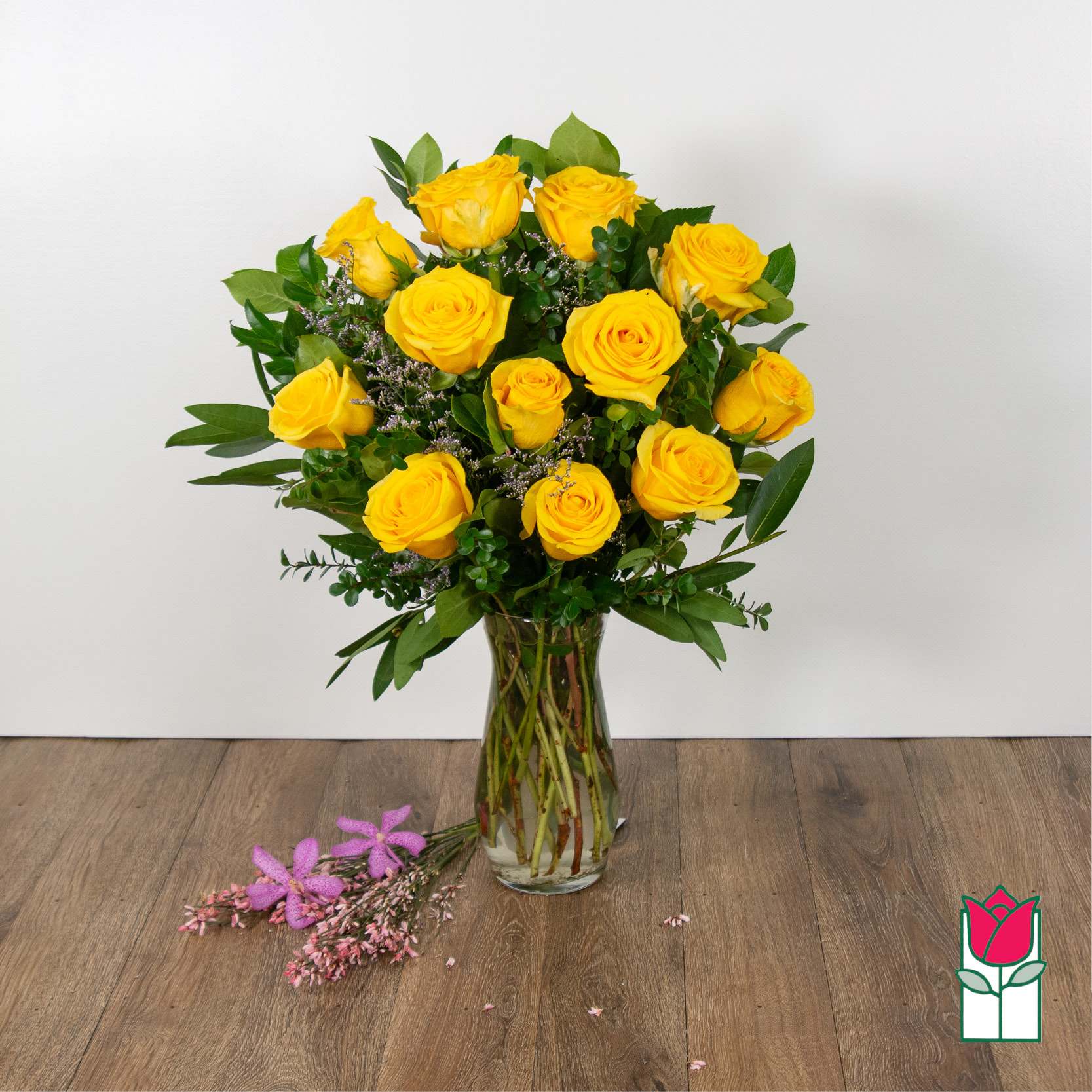 Yellow roses arranged in a clear glass vase with greenery