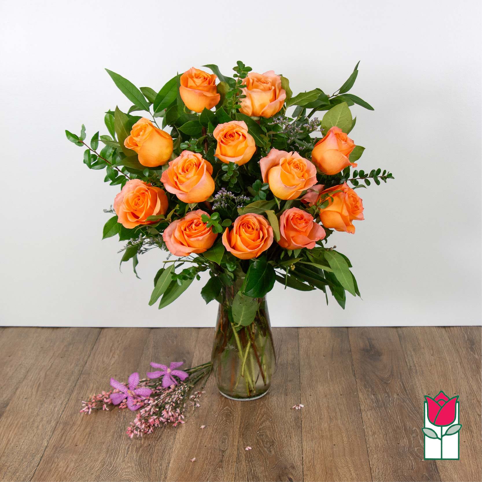 Orange roses arranged in a clear glass vase with greenery.