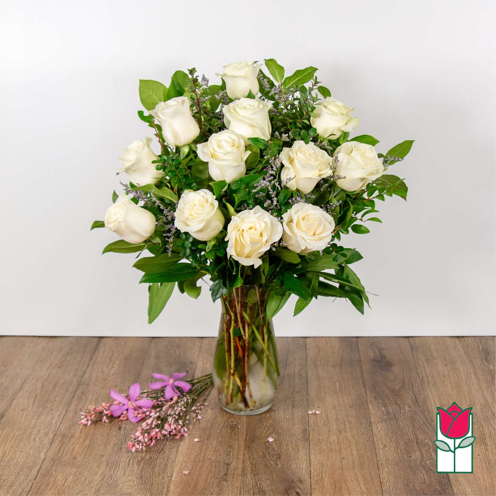 White roses arranged in a clear glass vase with greenery