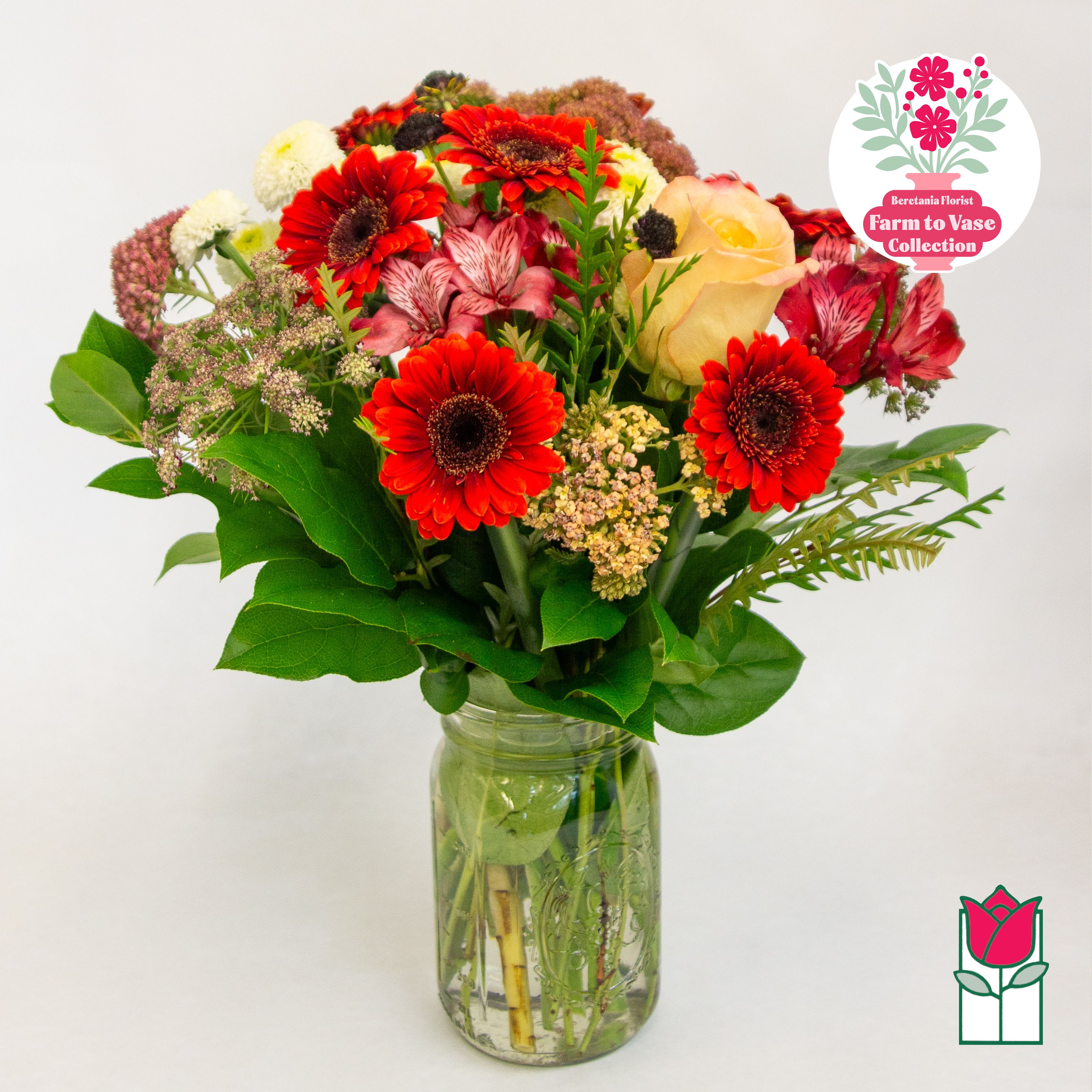 Mixed bouquet of red gerbera daisies and a peach rose in a glass jar vase