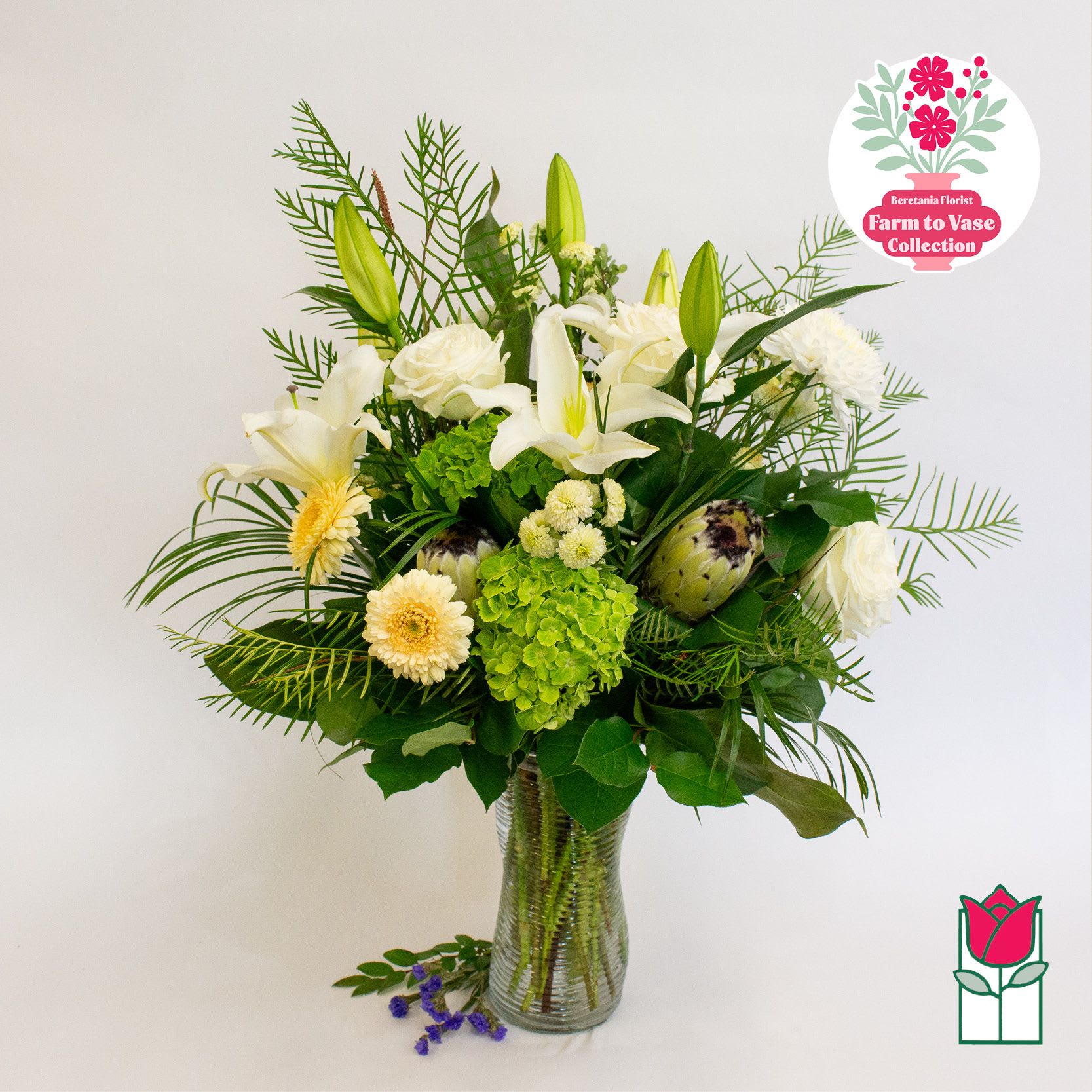 White lilies and cream flowers in a glass vase with green foliage