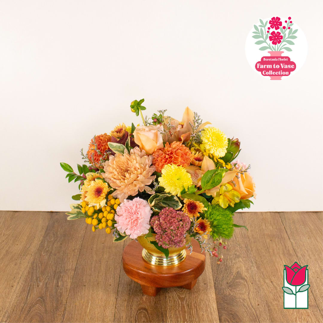 Mixed bouquet of peach, yellow, pink, and orange flowers in a gold vase