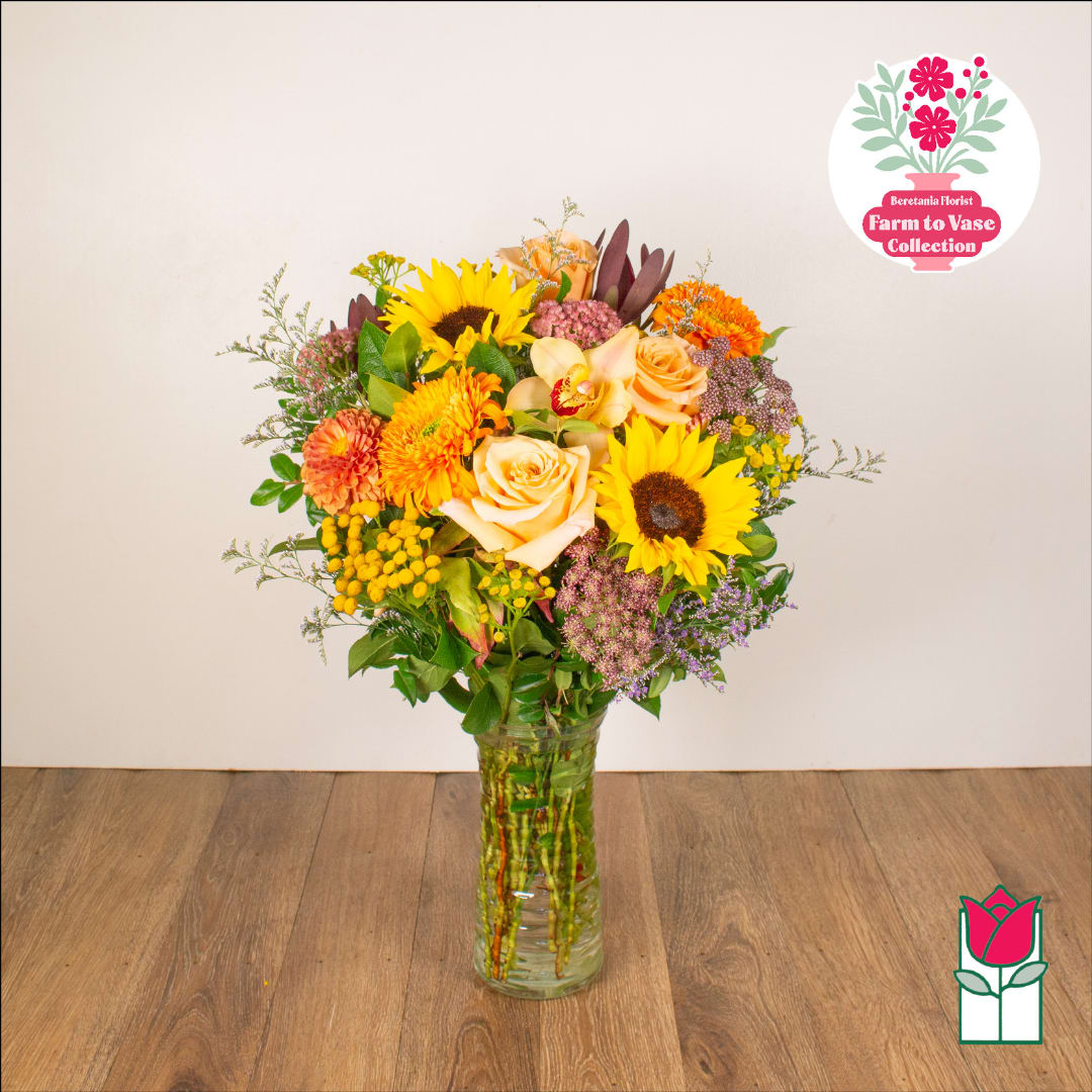 Mixed bouquet of sunflowers, roses, and orange blooms in a glass vase