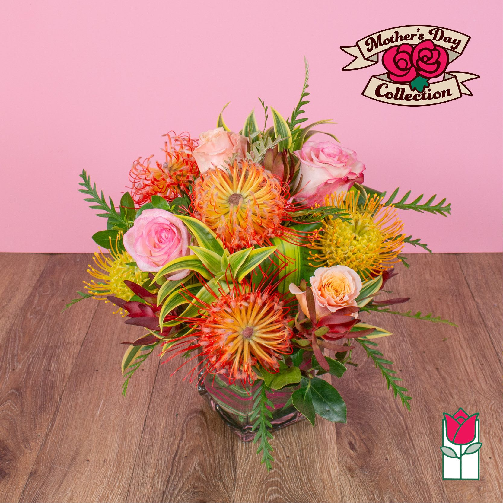 Arrangement of orange and yellow protea with pink roses in a square glass vase on a wooden surface