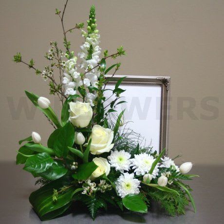 White floral arrangement with roses, tulips, and daisies in a framed display