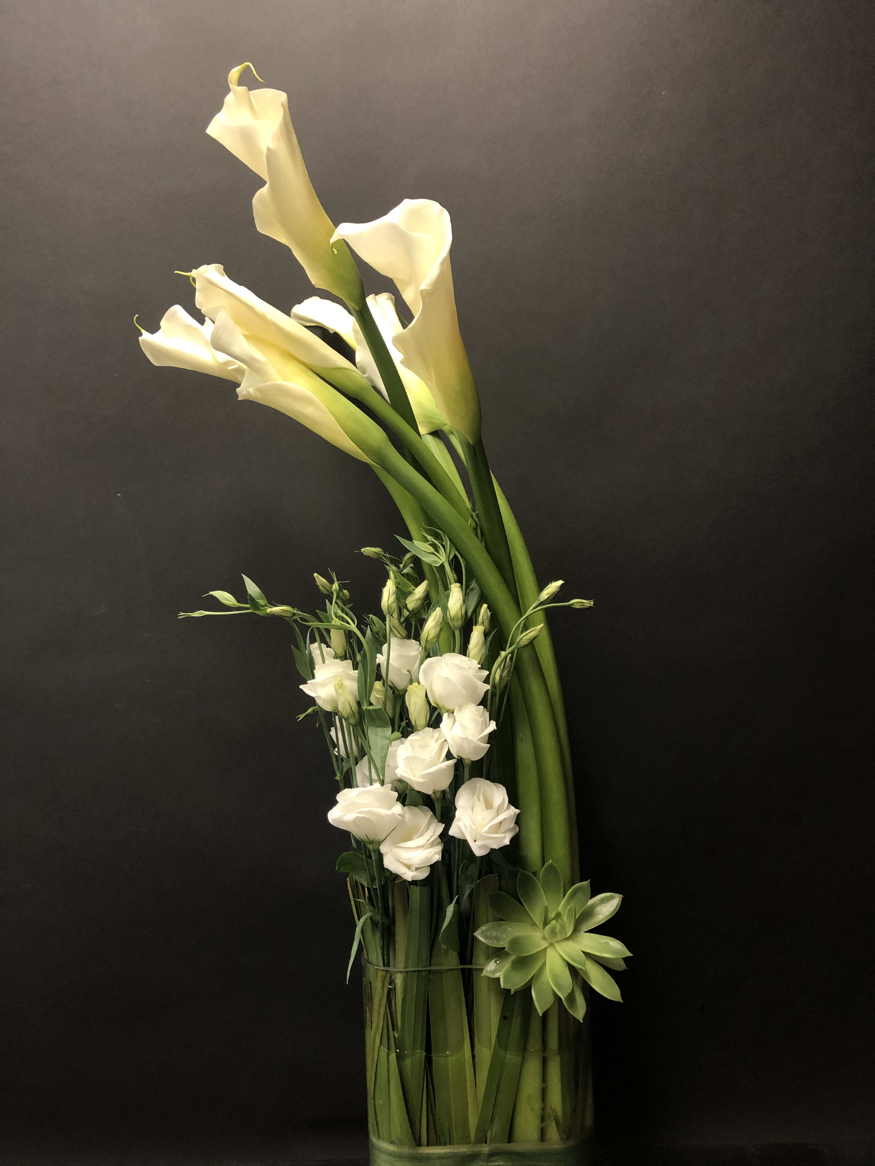 White calla lilies and small white blooms in a glass vase