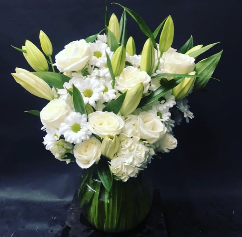 White roses and lilies arranged in a green glass vase
