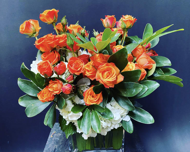 Orange roses arranged in a clear glass vase with white flowers