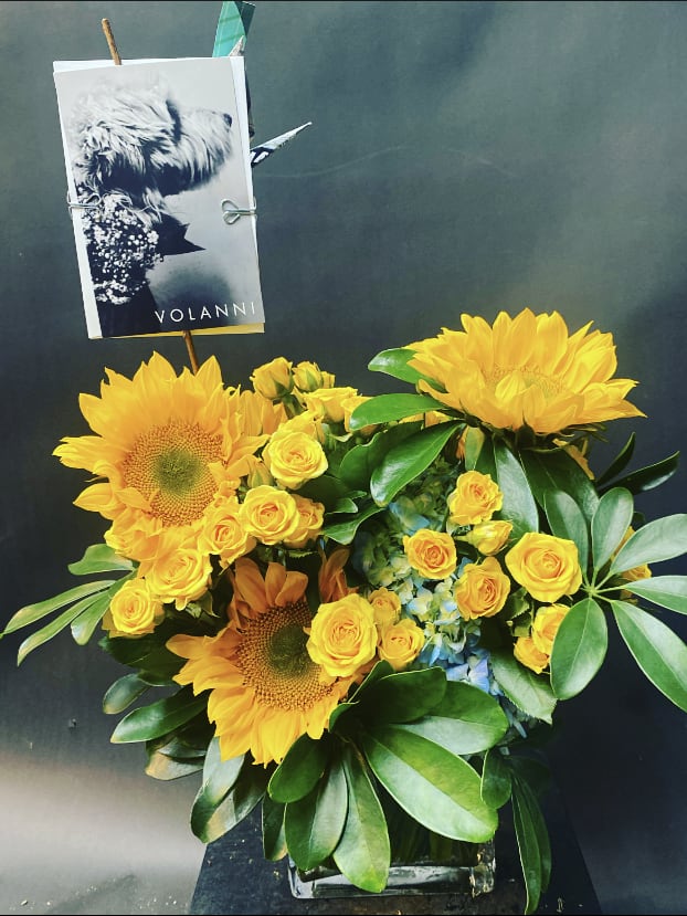 Yellow sunflowers and roses in a glass vase with a card pick