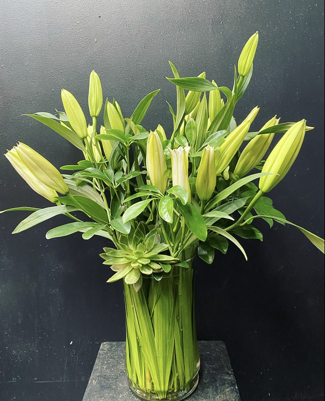 Tall arrangement of unopened yellow lilies in a glass vase