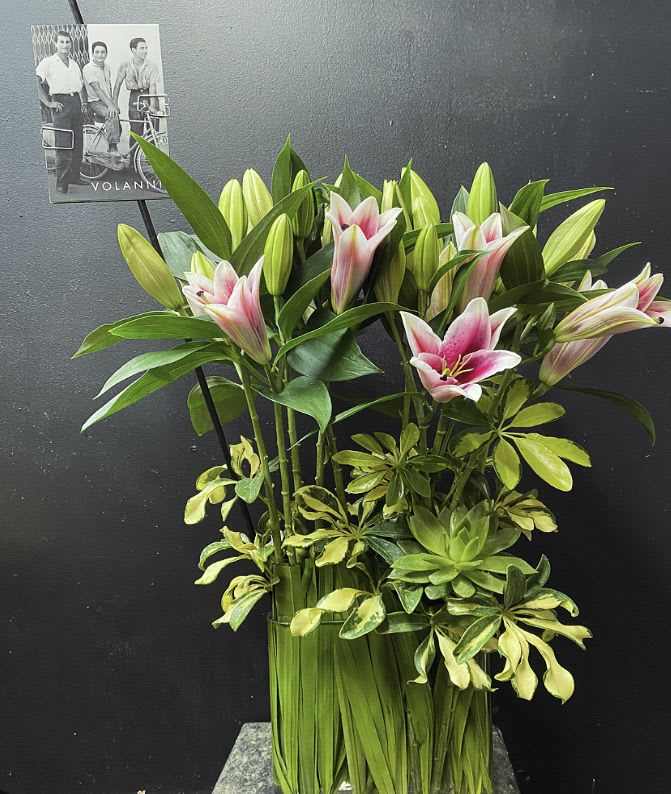Pink and white lilies arranged with variegated greenery in a tall vase
