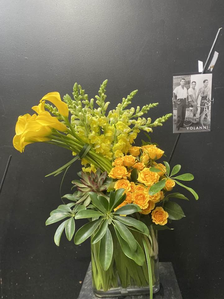 Yellow calla lilies and roses in a glass vase with greenery