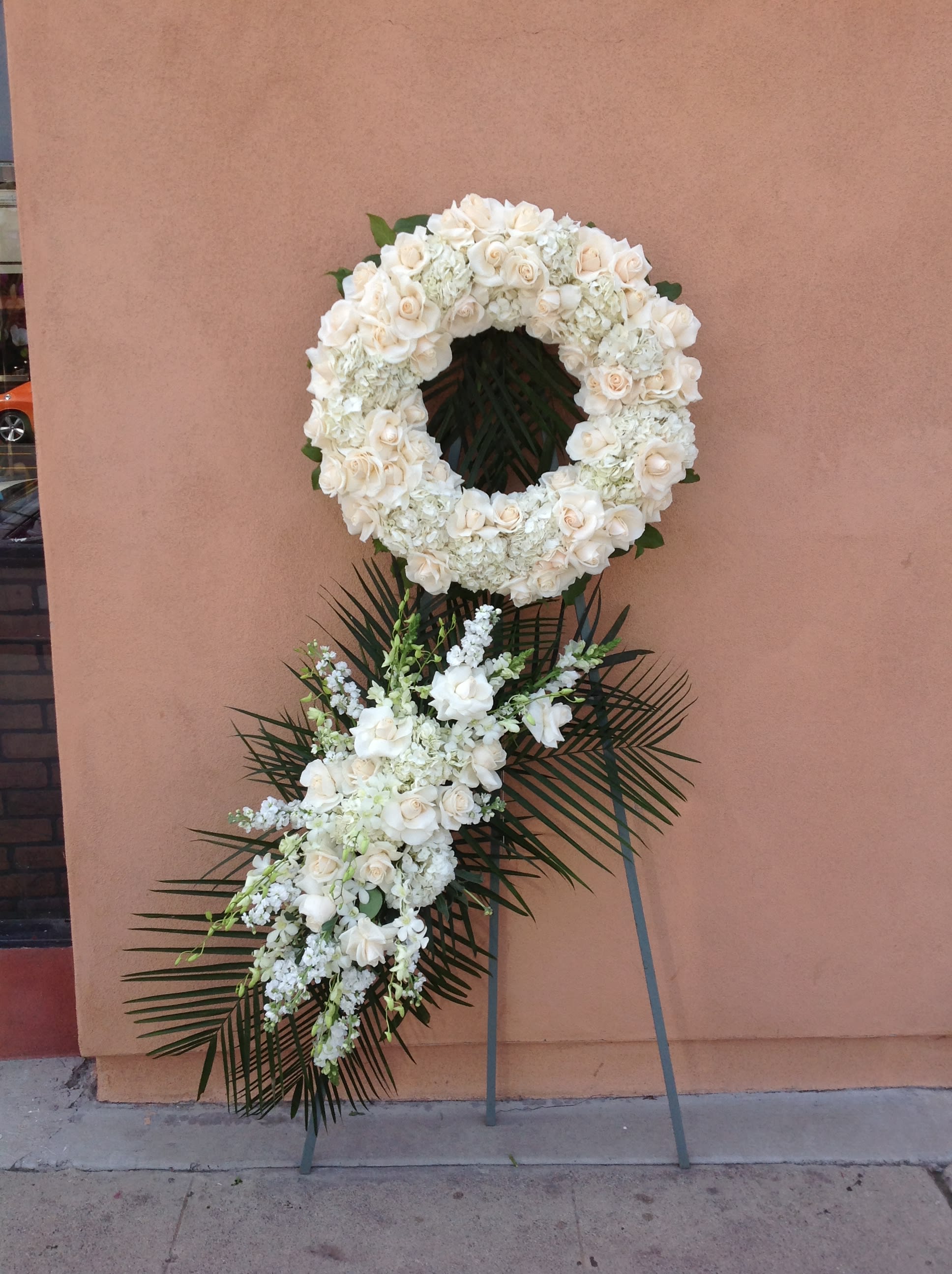 White floral wreath and spray on a stand with palm fronds