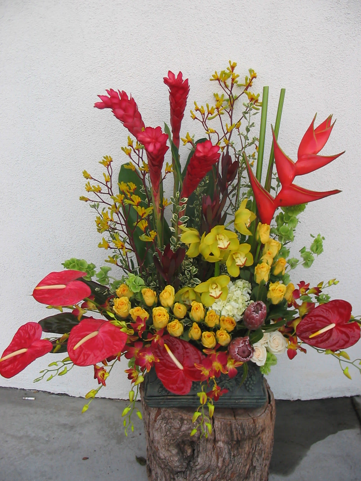Tall tropical flower arrangement with red anthuriums, yellow orchids, and red heliconia
