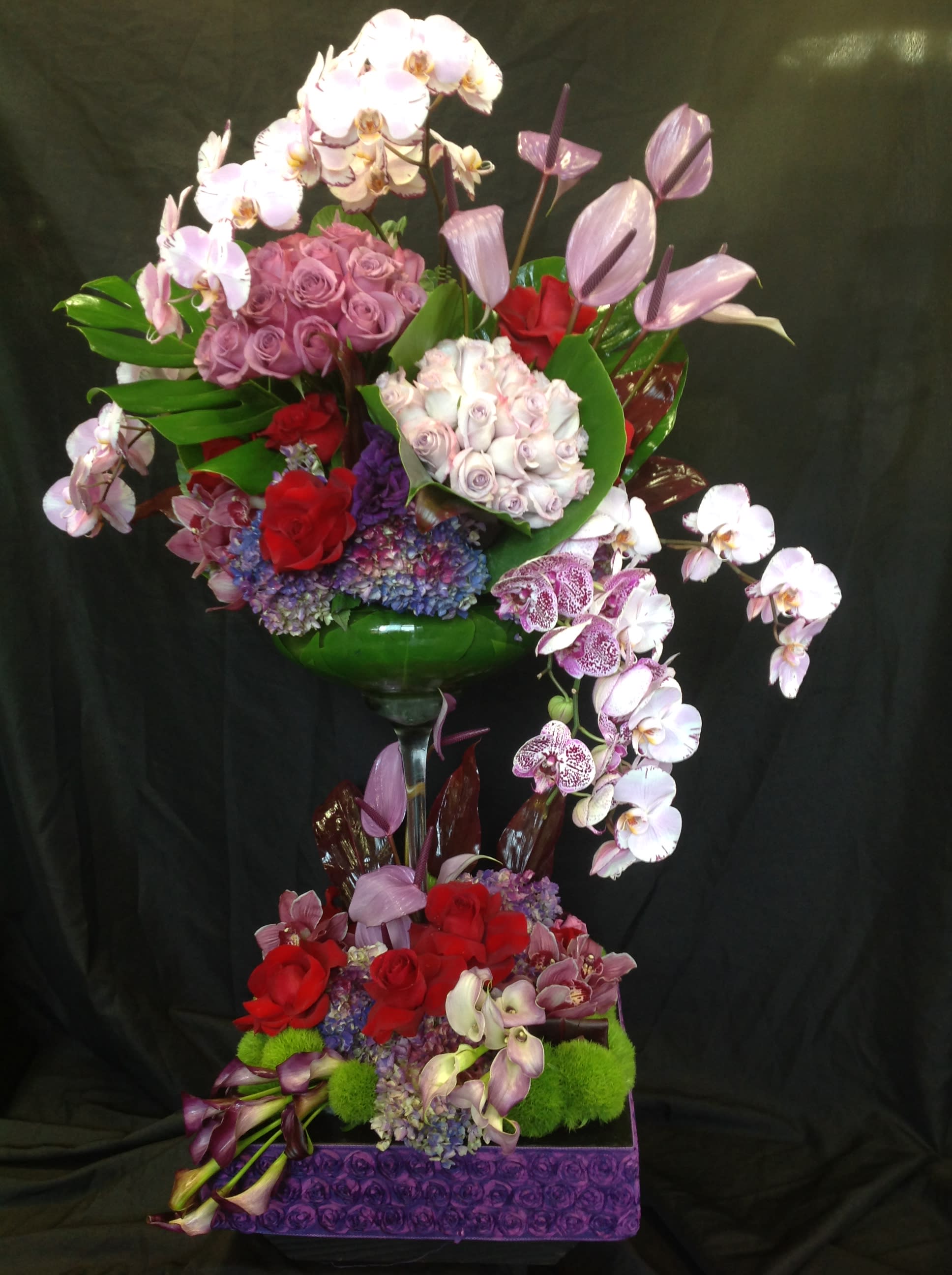 Tall floral arrangement with orchids, roses, and hydrangeas in a glass vase