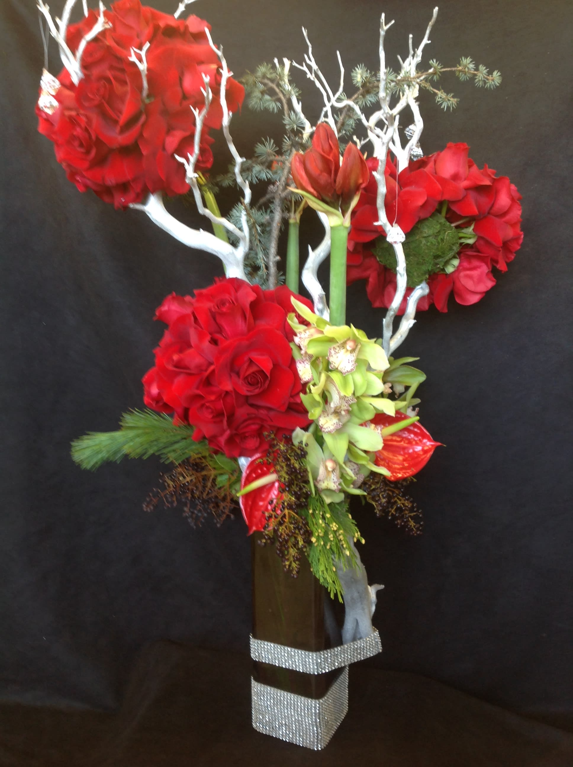 Tall floral arrangement with red roses and orchids in a square vase