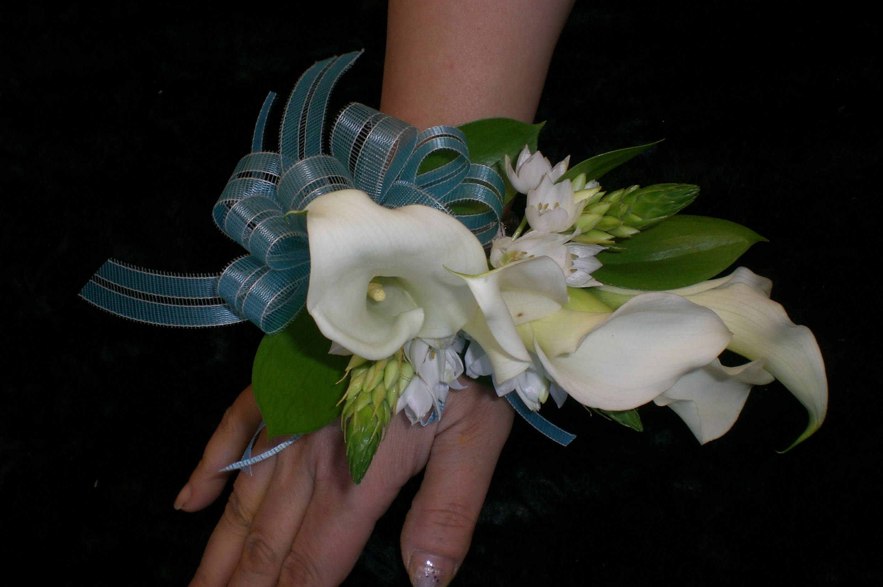 White calla lily corsage with blue ribbon and green leaves