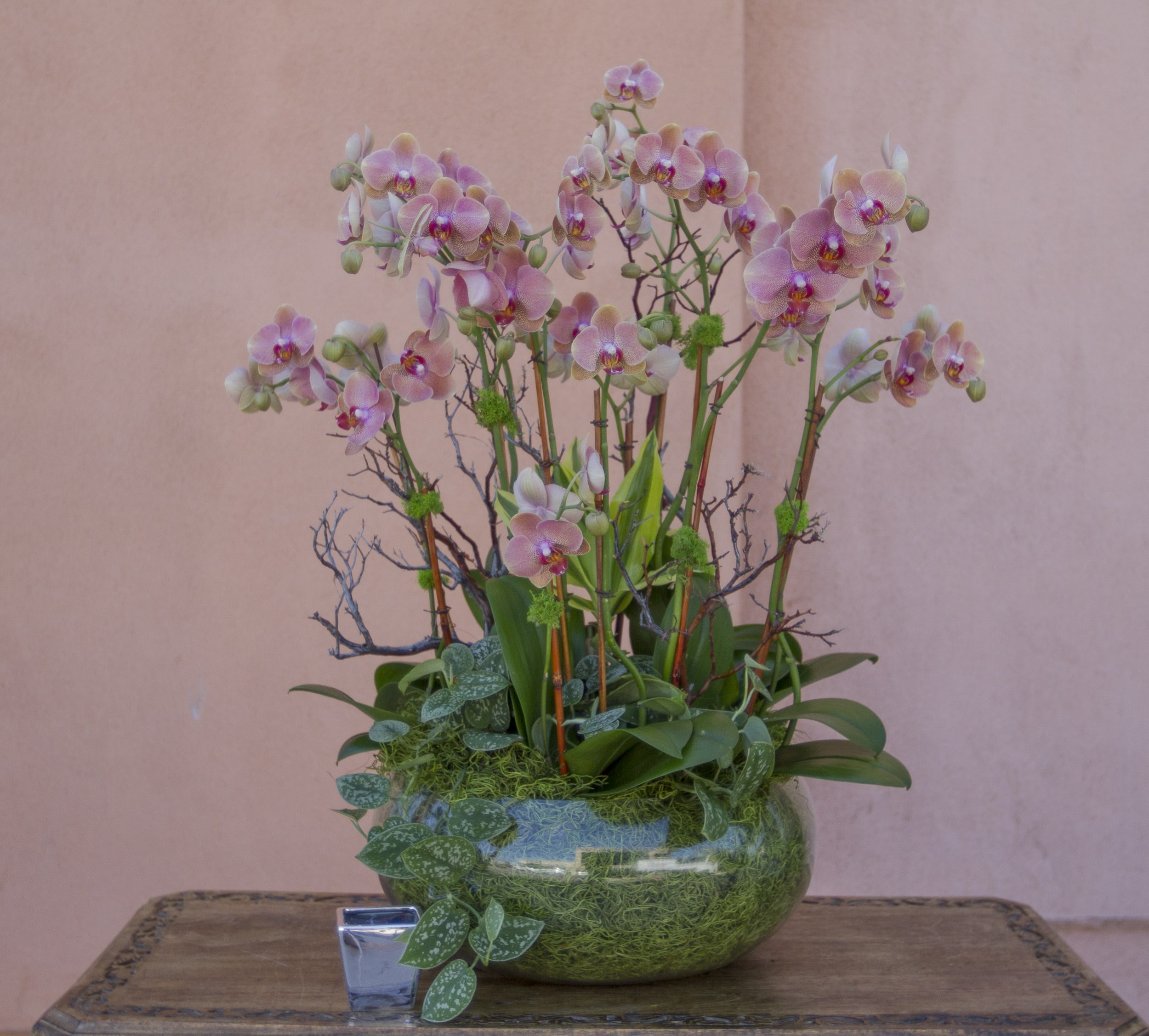 Pink orchid arrangement in a glass bowl with trailing greenery