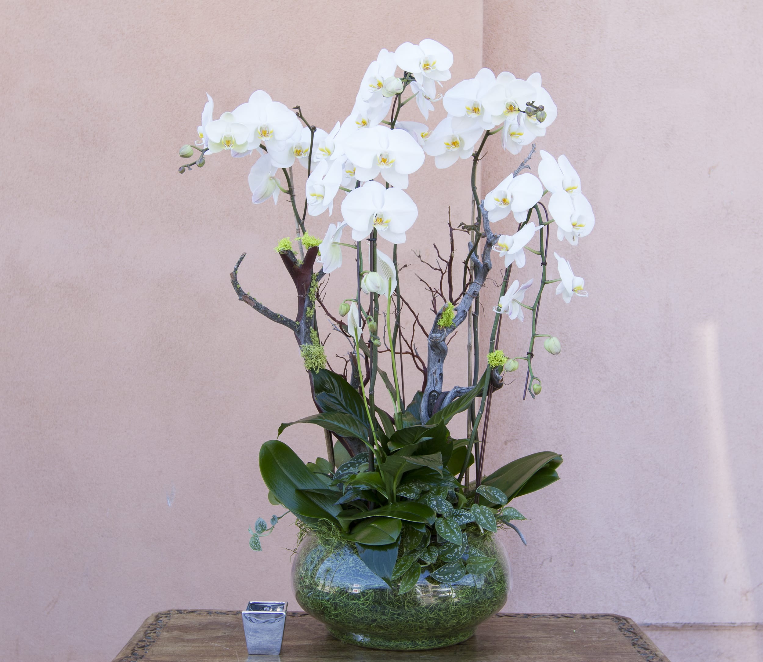 White orchid arrangement in a glass bowl vase on a table