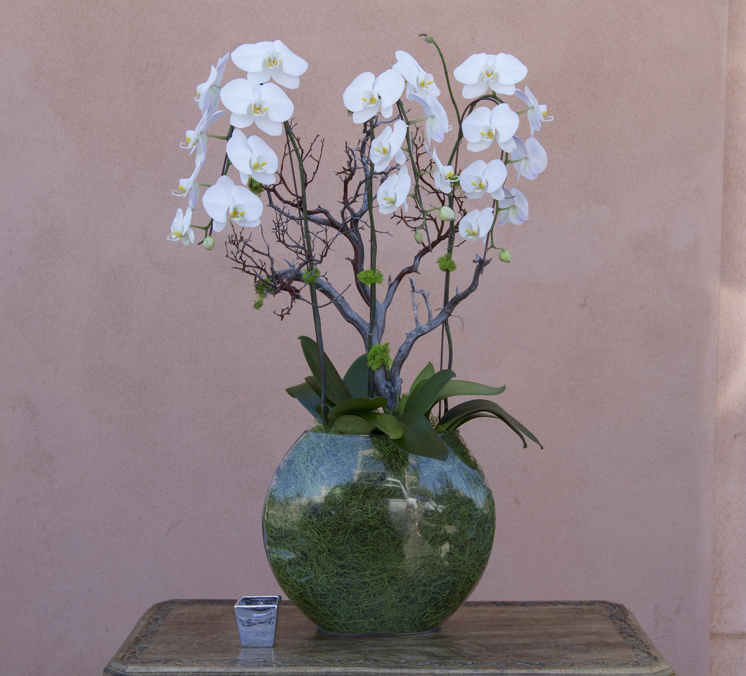White orchid arrangement in a round green glass vase with a small candle holder beside it