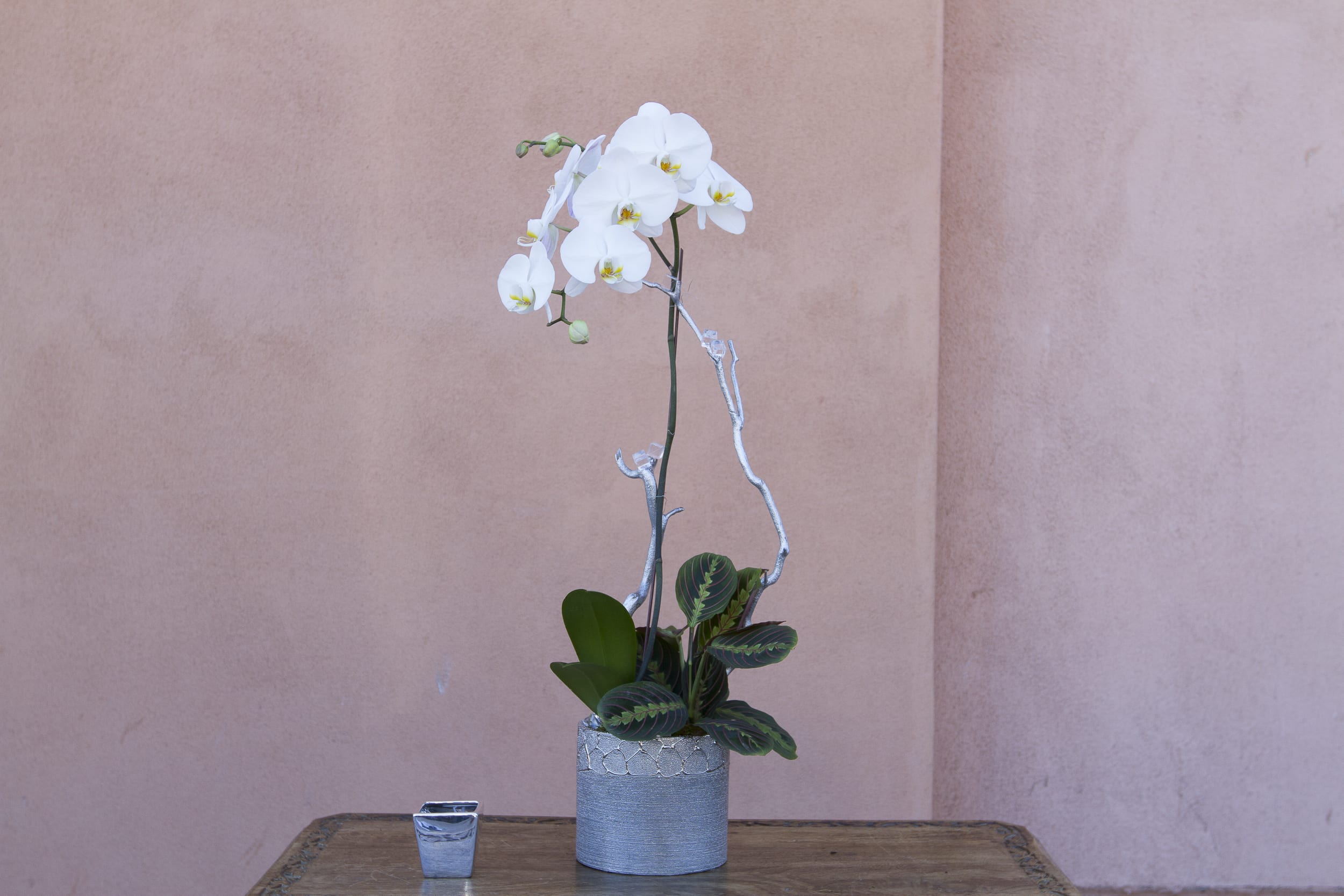 White orchid arrangement in a silver pot with a small candle beside it