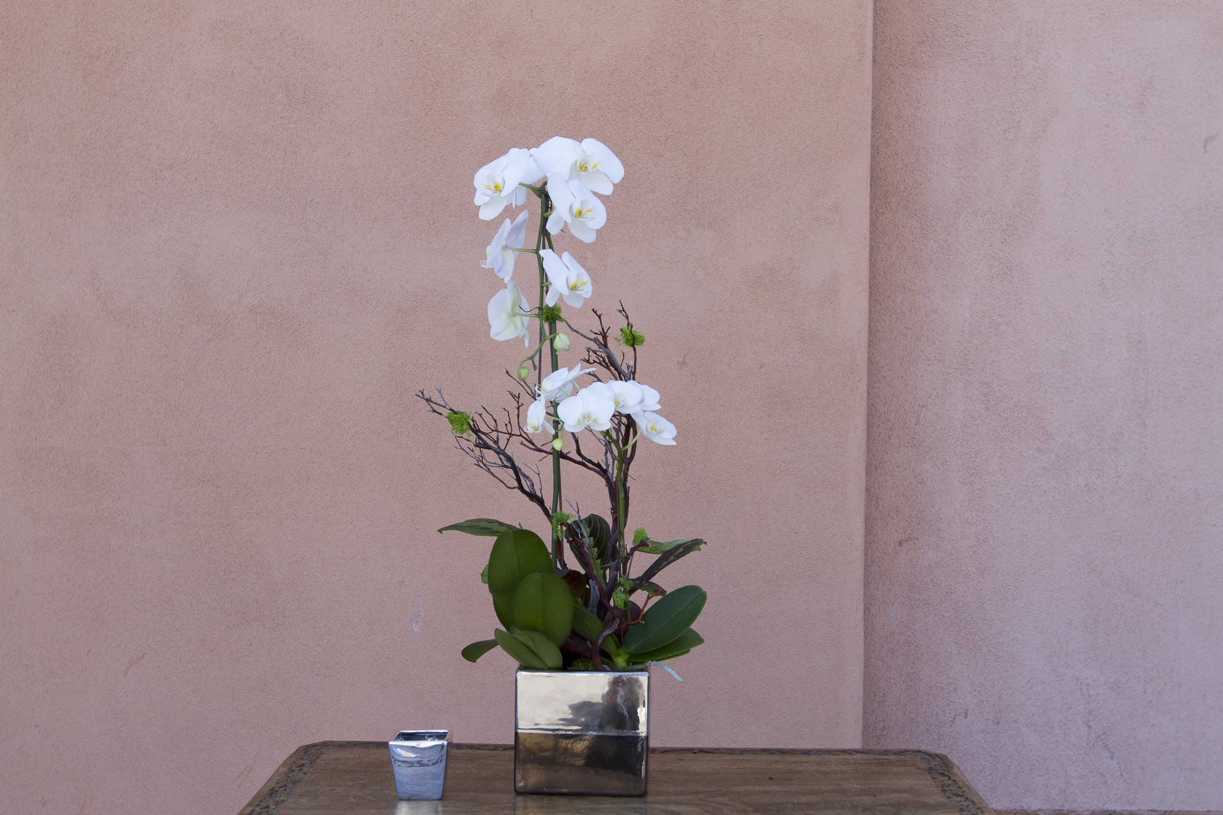 White orchid arrangement in a square silver vase with a small candle beside it