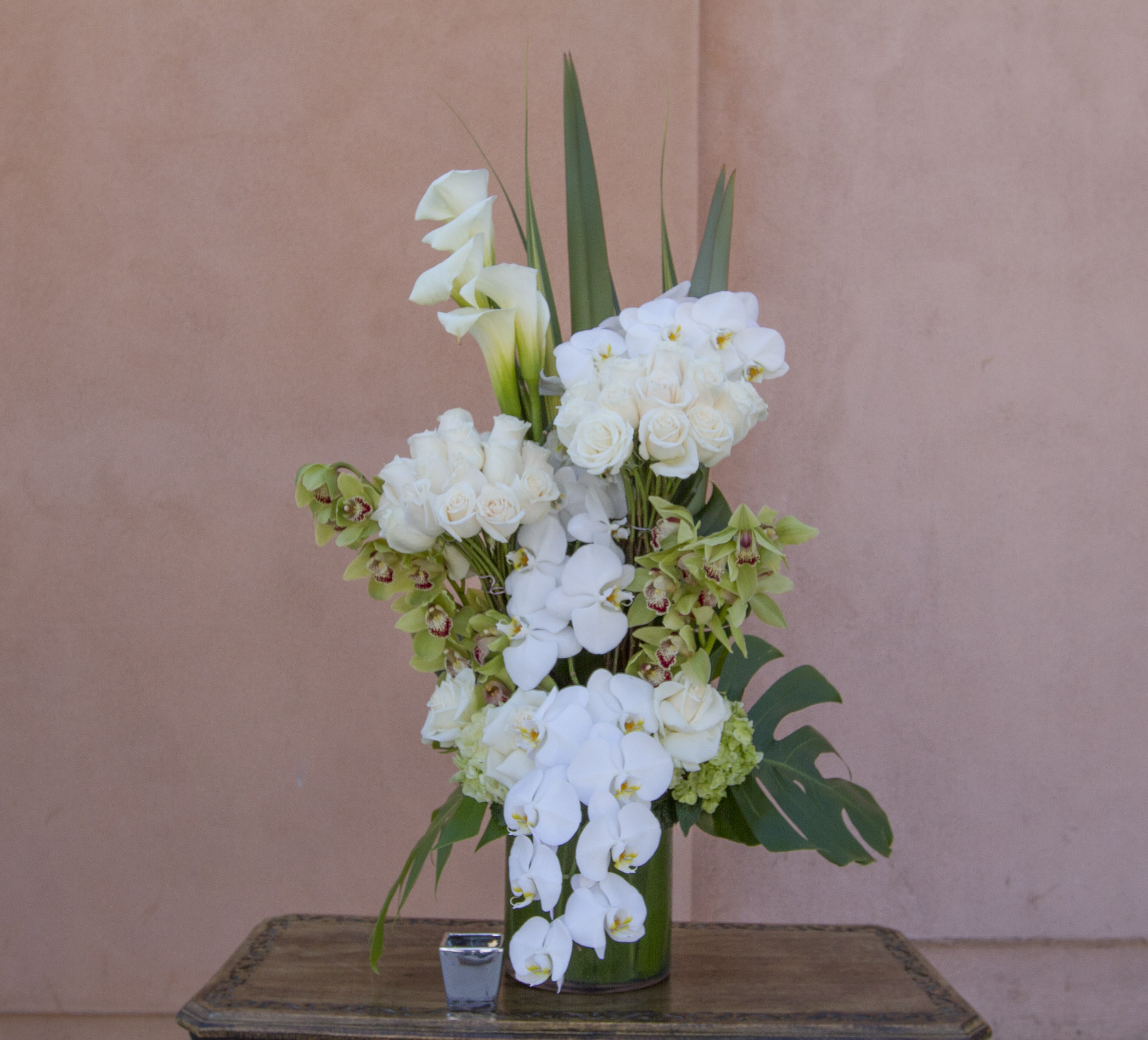 Tall white floral arrangement in a green vase with calla lilies and orchids