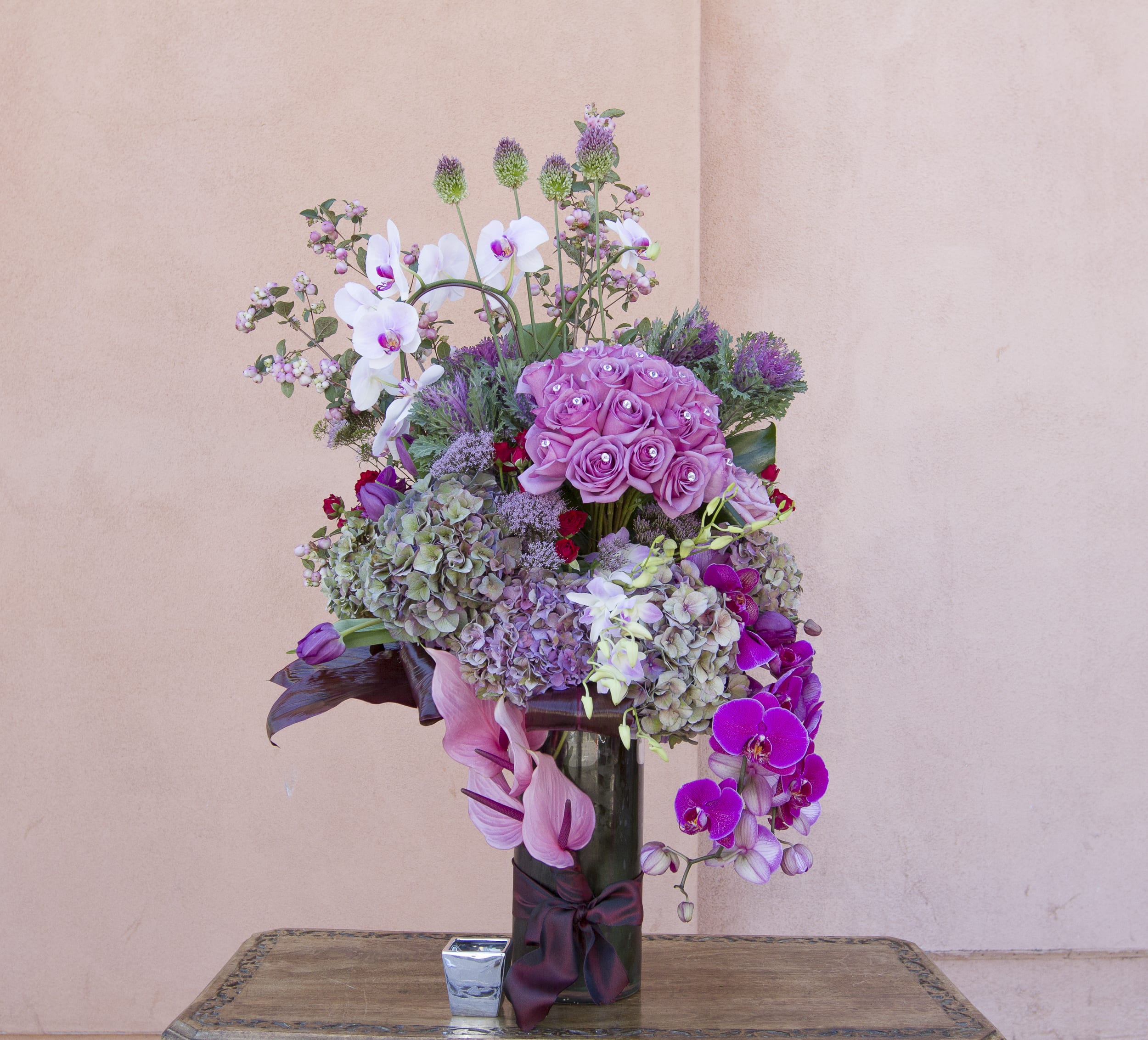 Tall bouquet of pink roses, orchids, and hydrangeas in a glass vase