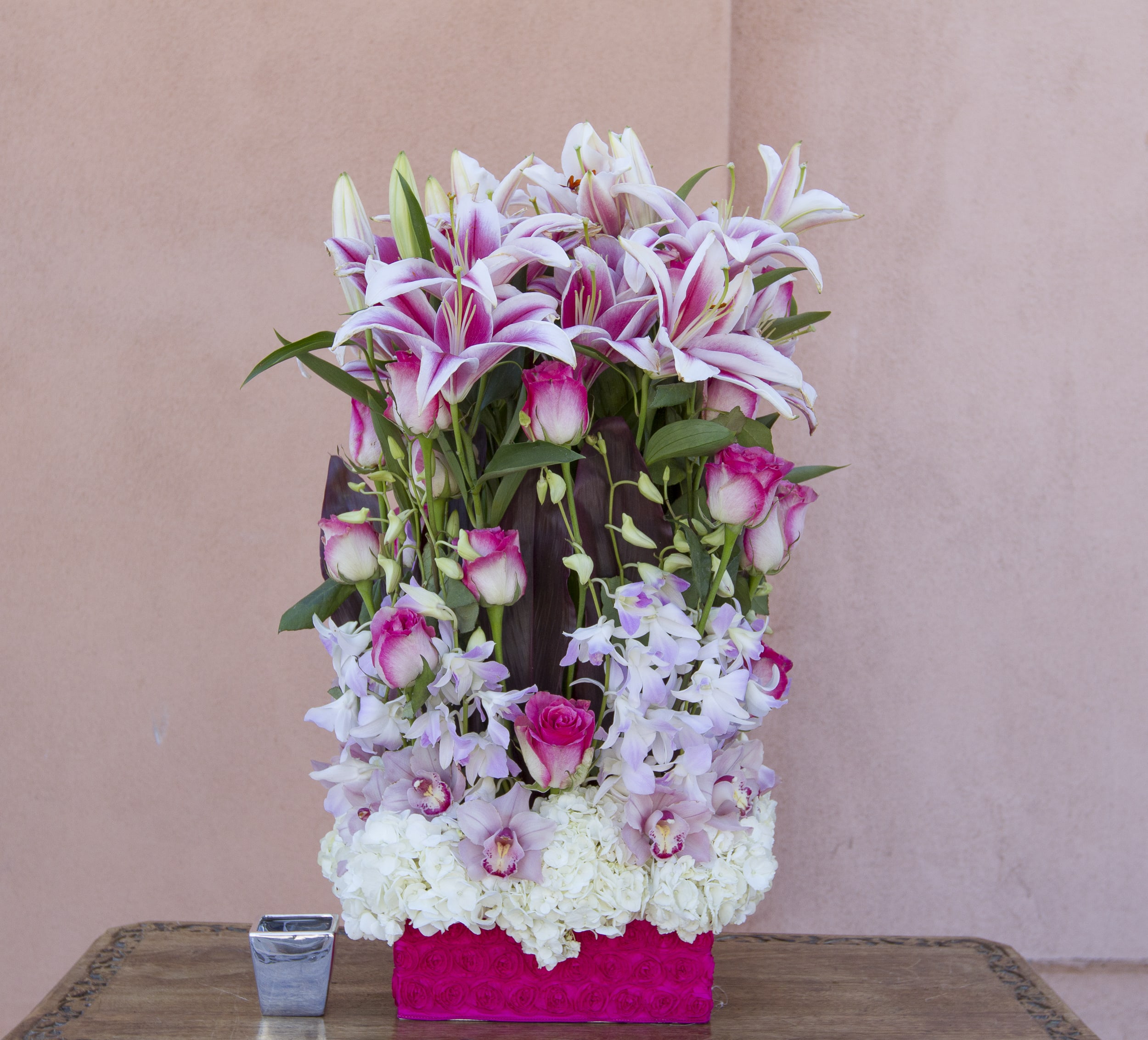 Tall floral arrangement with pink lilies, roses, orchids, and white hydrangeas in a pink box