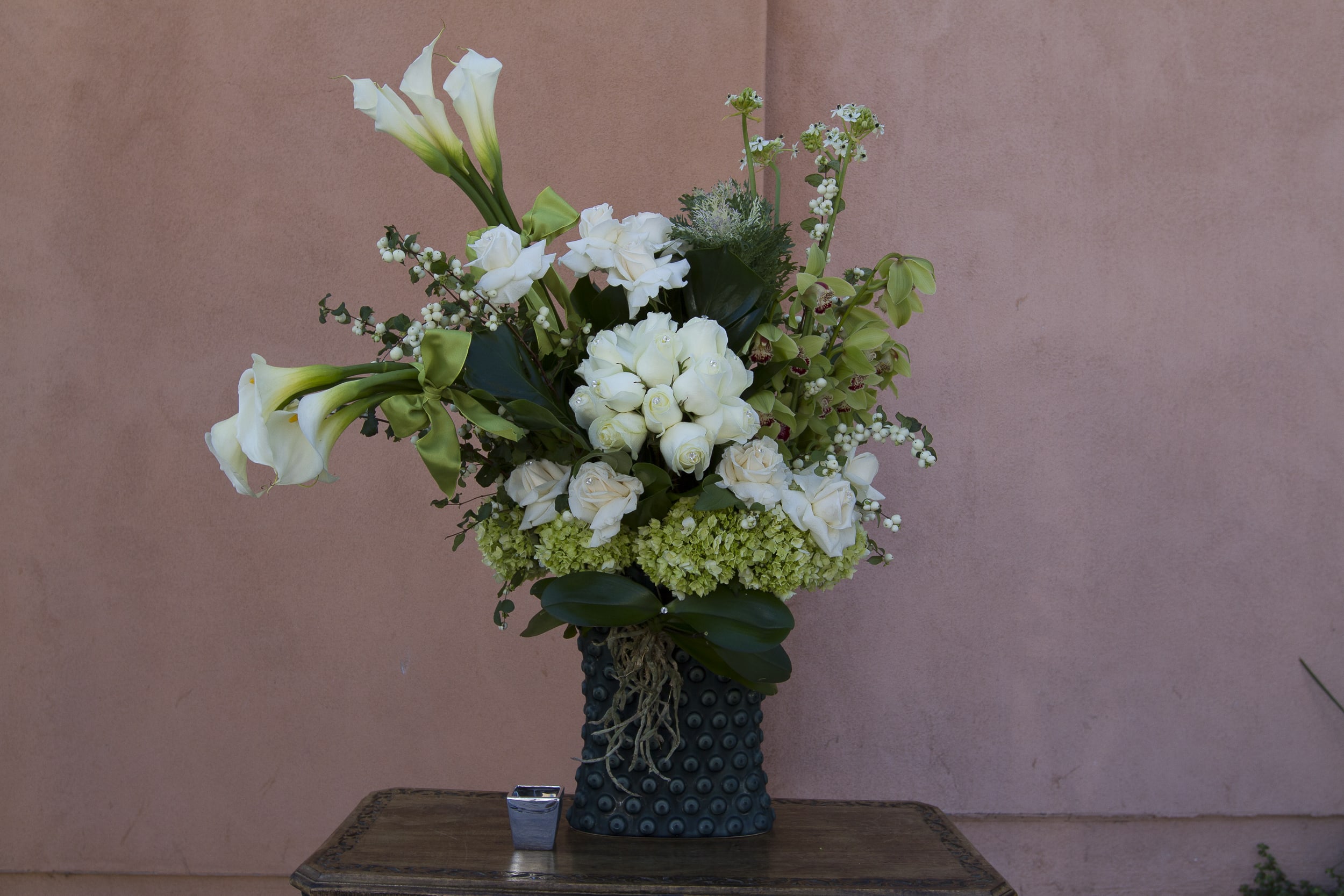 White calla lilies and roses arranged in a dark textured vase