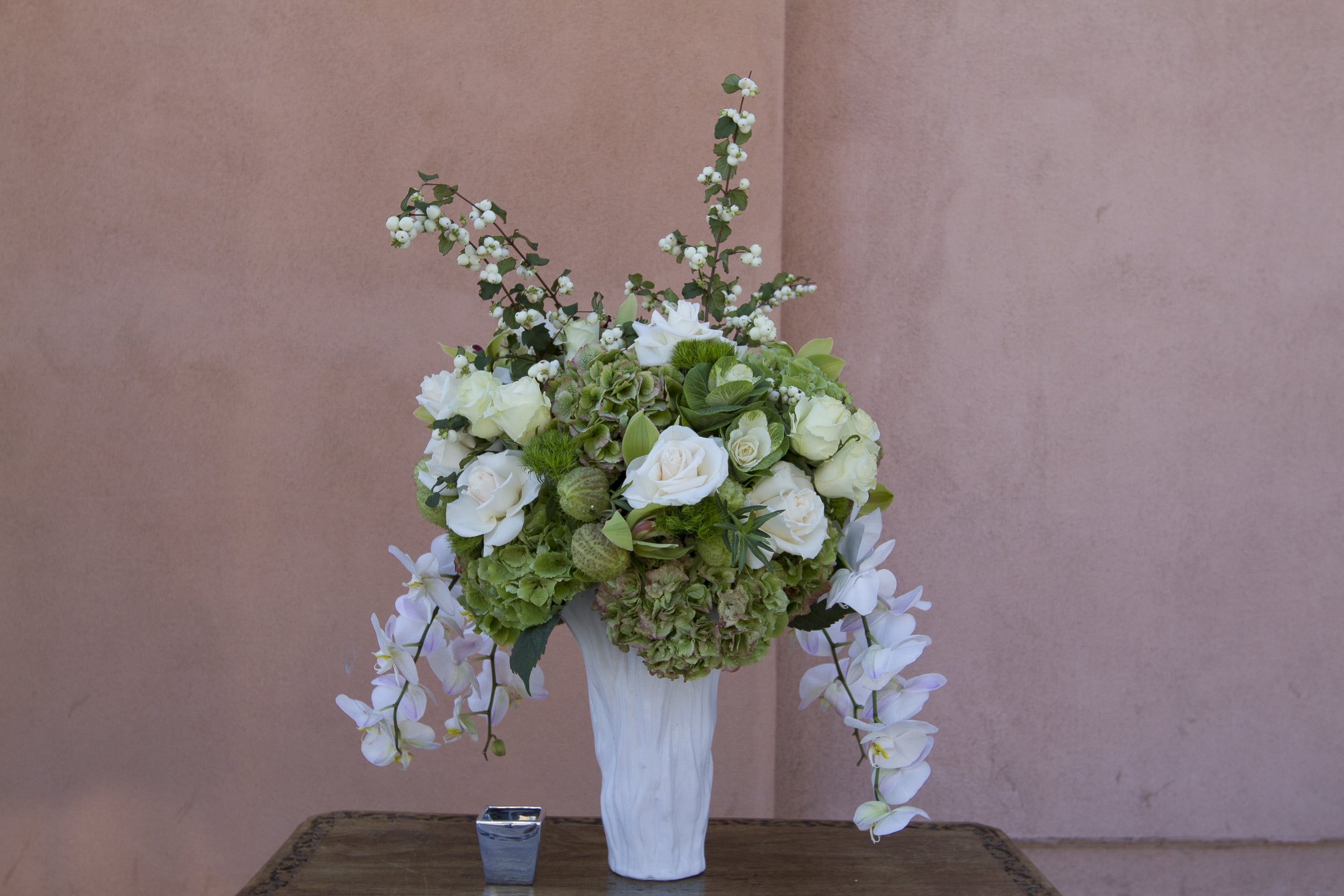 White and green floral arrangement in a tall white vase with trailing orchids