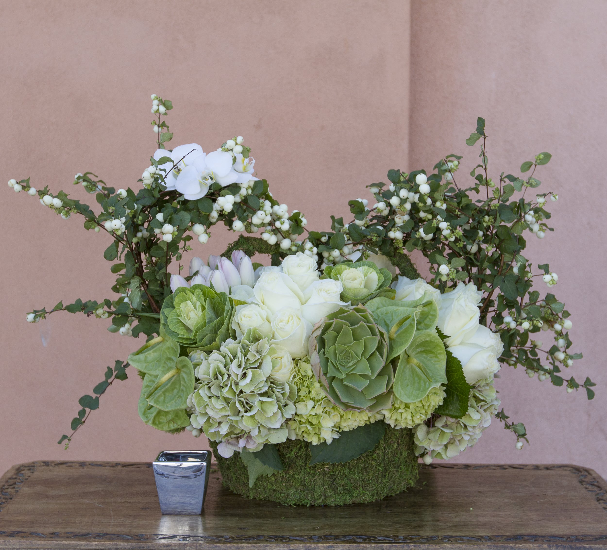 White and green floral arrangement in a moss-covered container