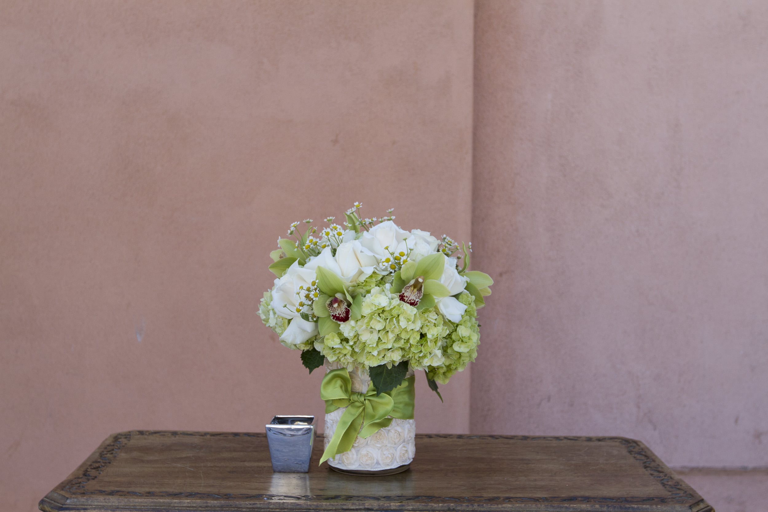 White and green floral arrangement in a decorated vase with a green ribbon
