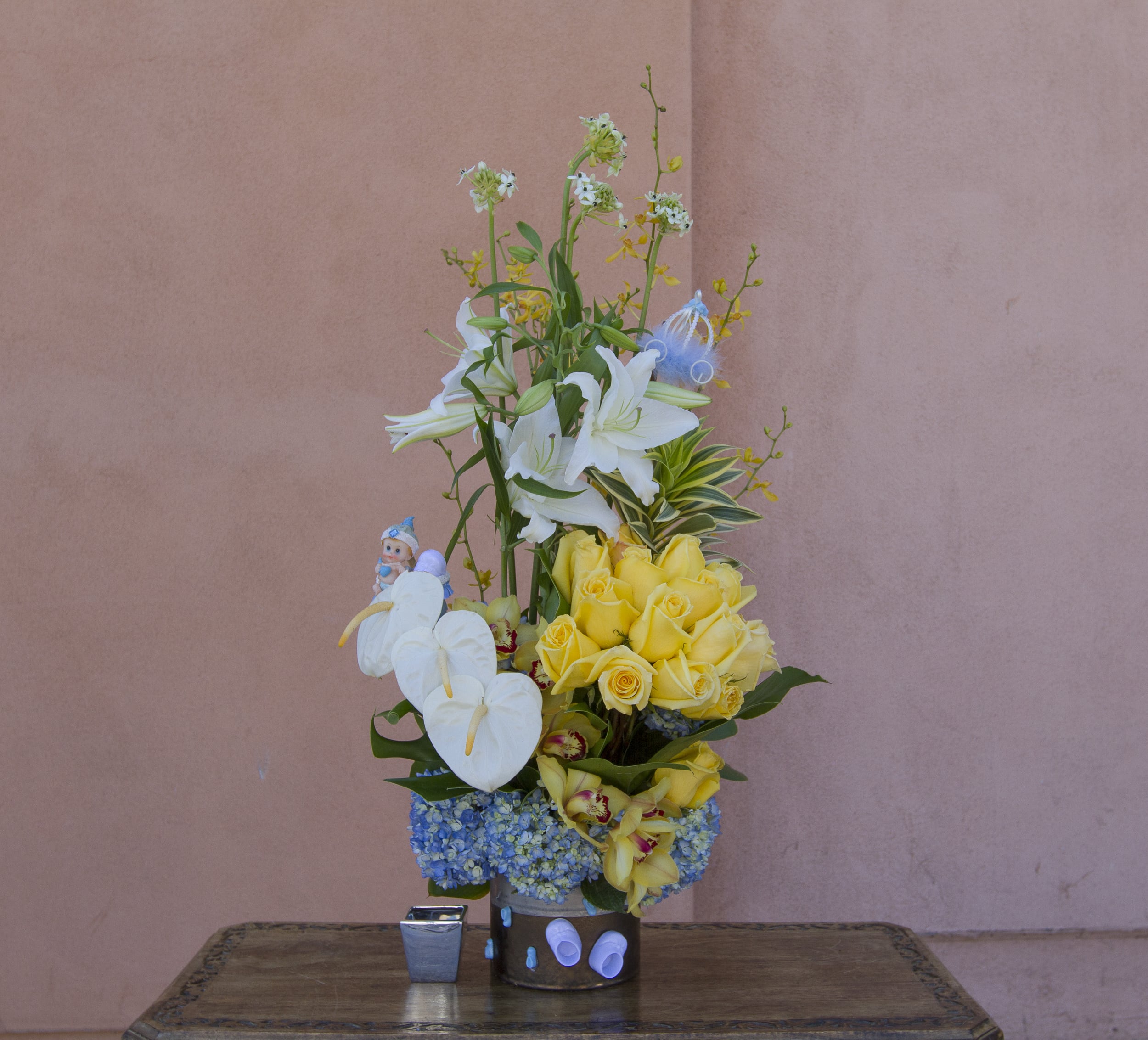 Tall floral arrangement with white lilies, yellow roses, and blue hydrangeas in a container