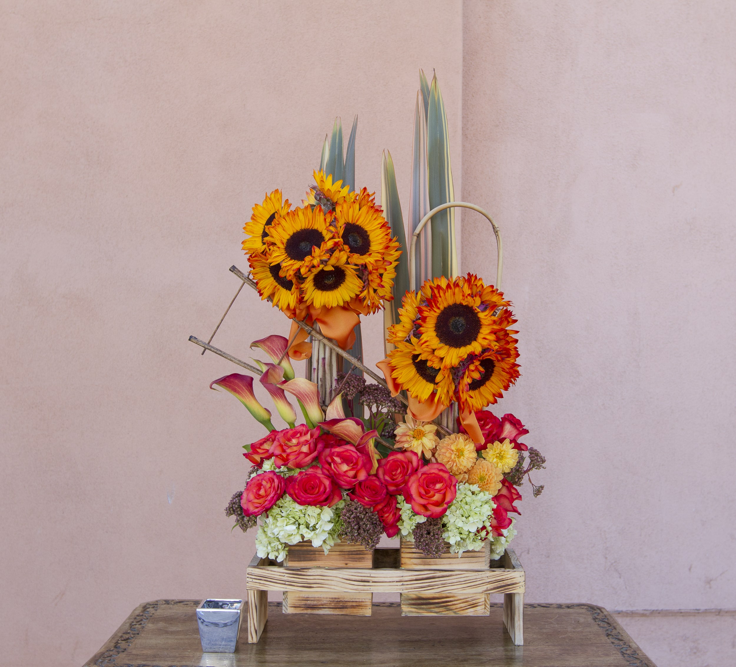 Tall floral arrangement with sunflowers, roses, and calla lilies in a wooden stand