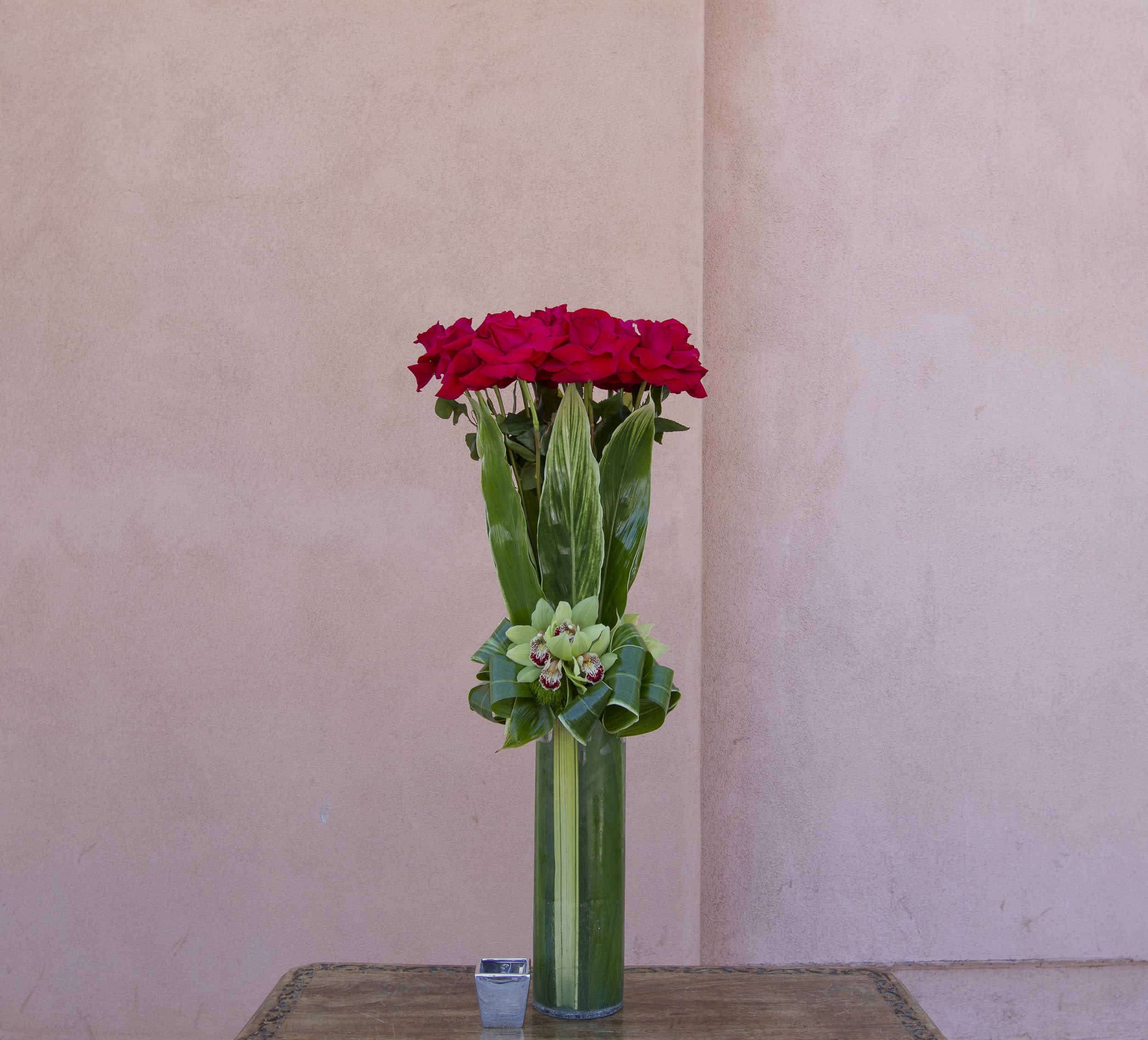 Tall vase arrangement of red roses with green orchids in a glass cylinder